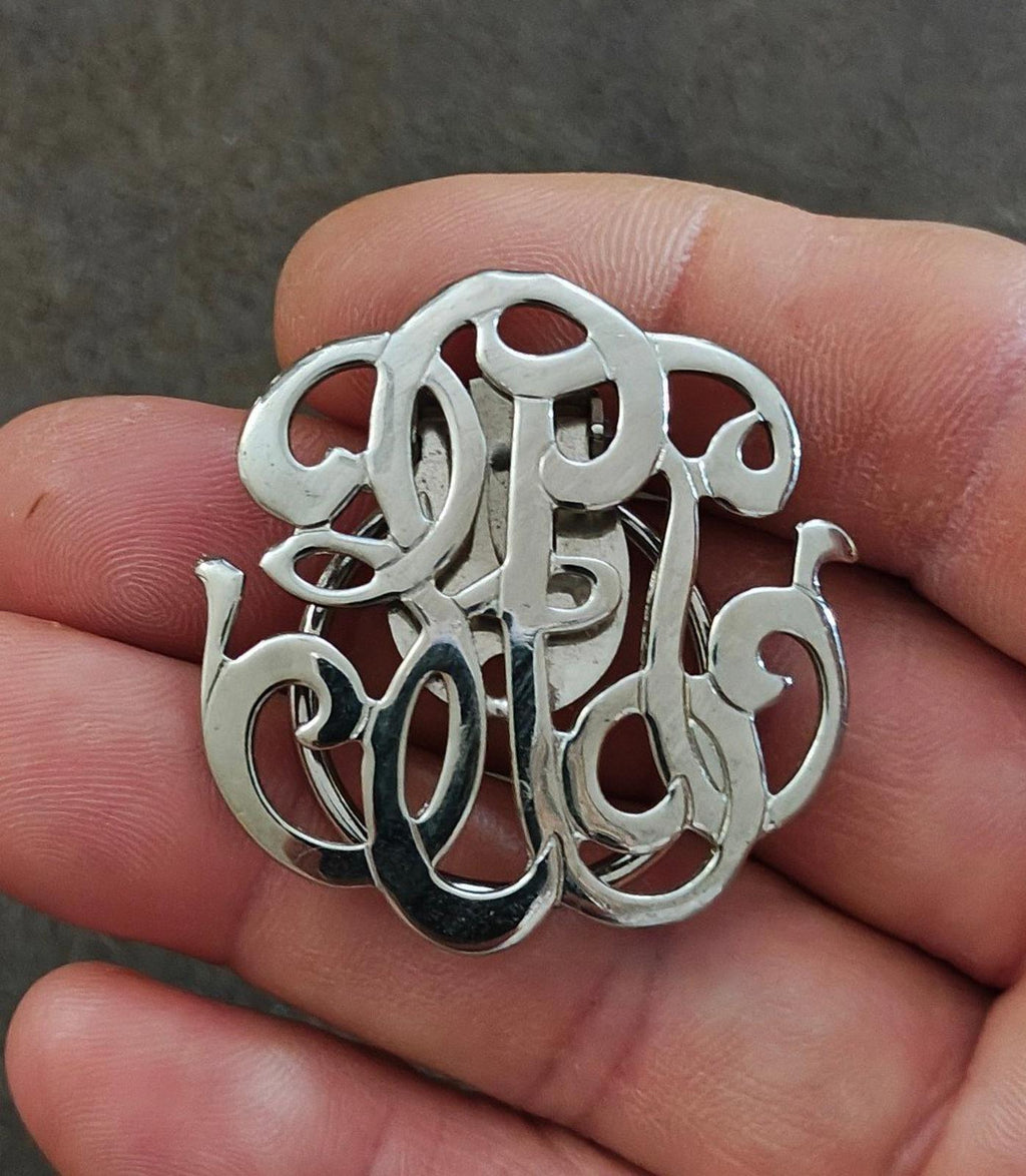 Silver-tone monogram scarf clip with ornate cutout lettering and polished details