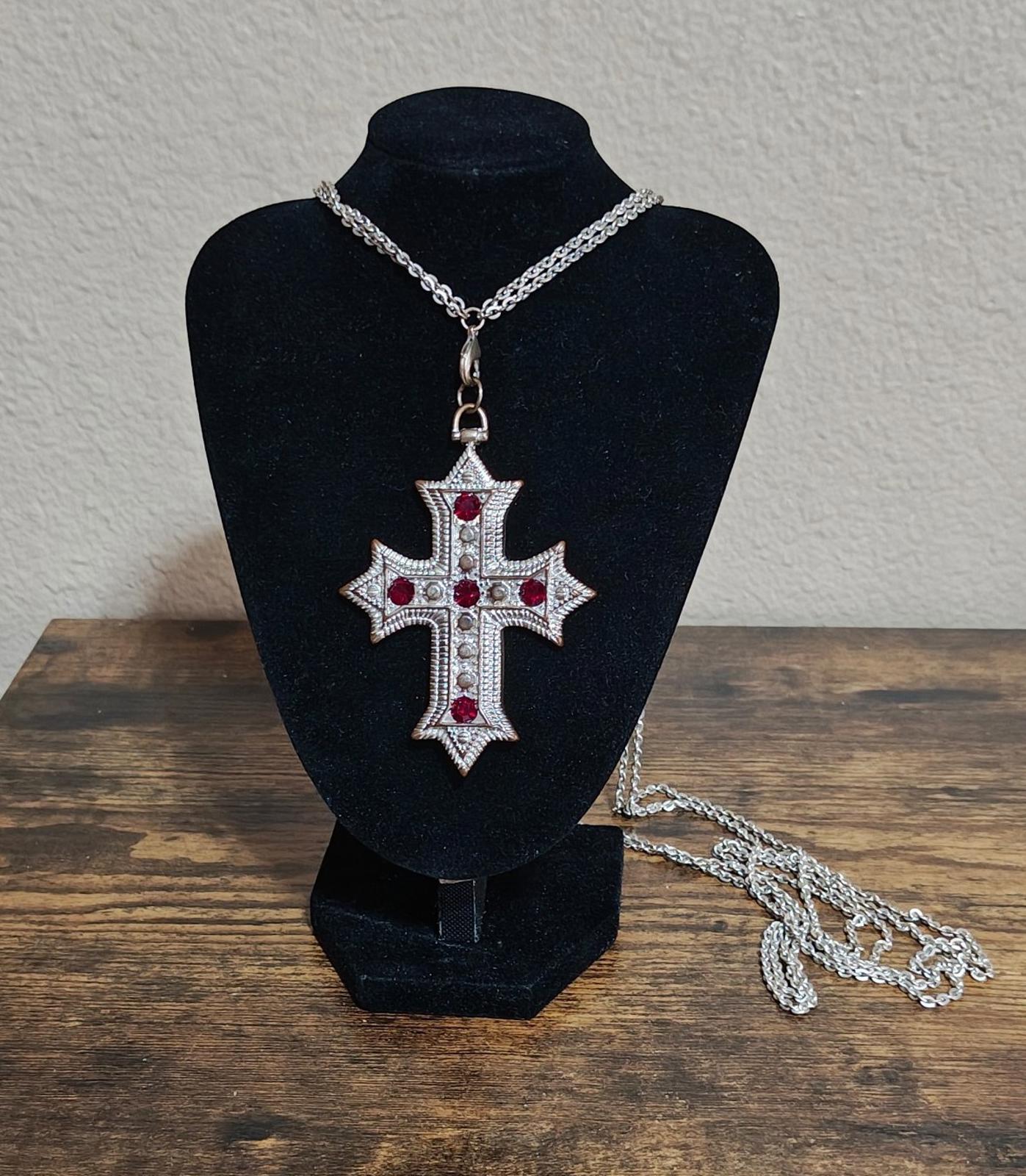 Silver tone cross pendant necklace with red rhinestones centered on a chain display