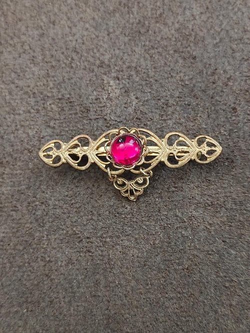 Gold-tone heart-shaped brooch pin with openwork sides and center red cabochon