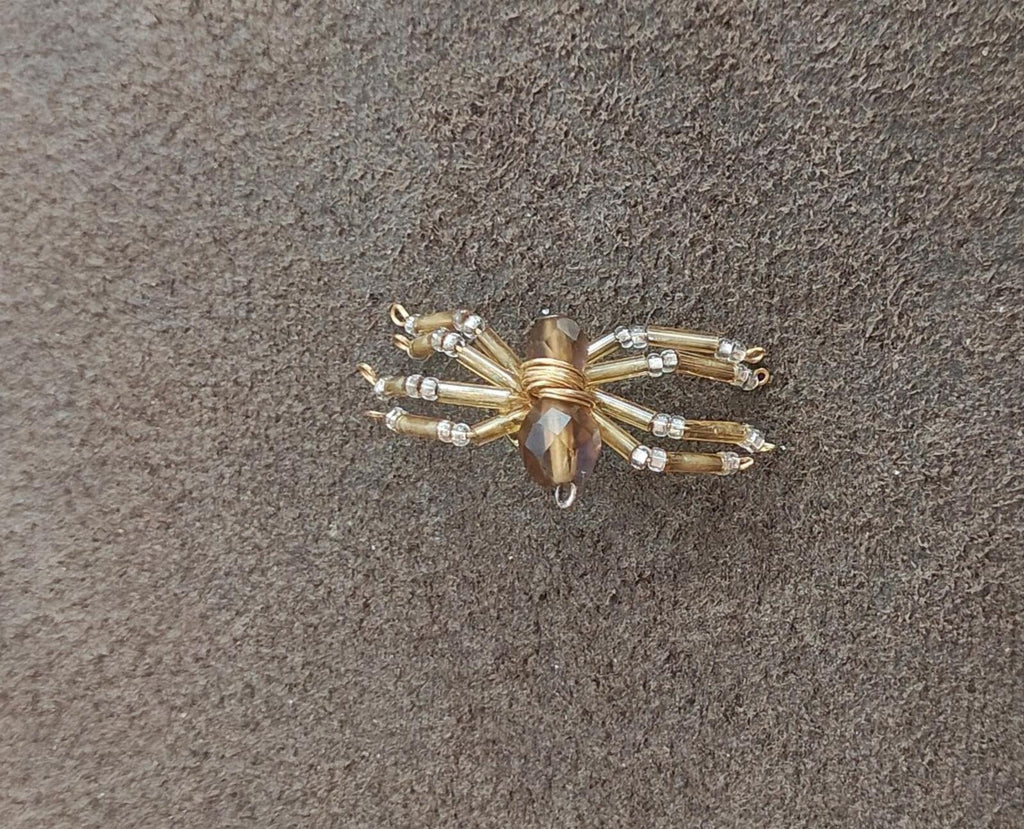 Gold-toned beaded spider pin with faceted amber center and crystal bead legs.