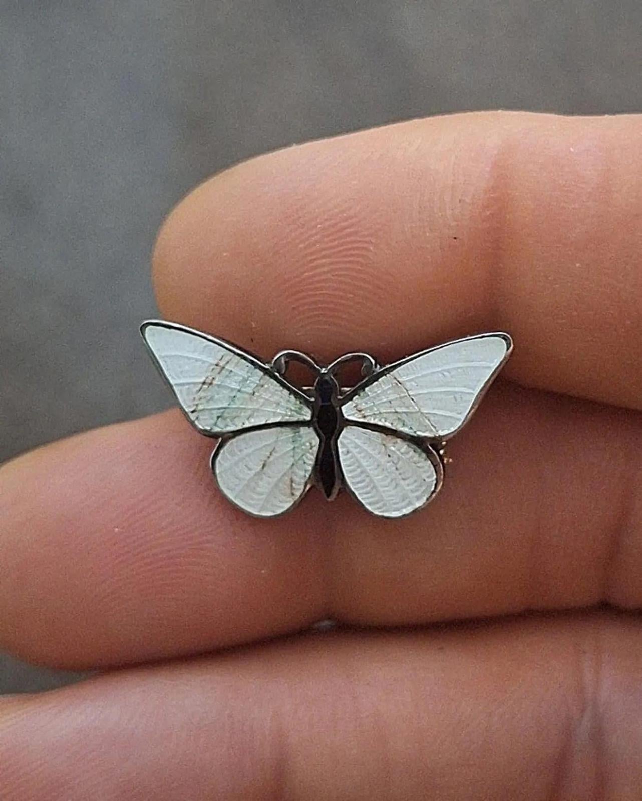 Enamel butterfly pin brooch with white wings and dark body, shown on fingertip.