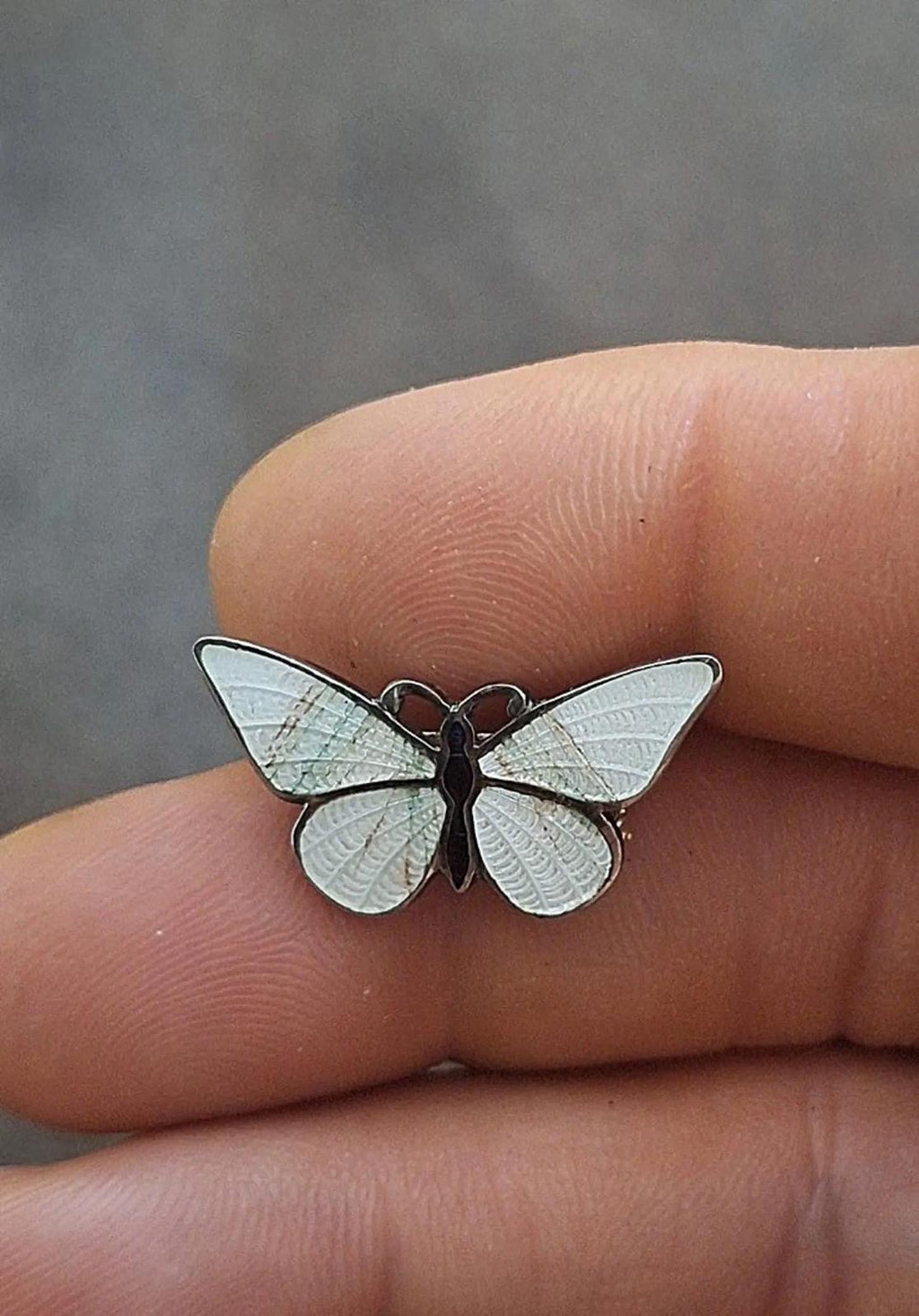 Enamel butterfly pin brooch with iridescent white wings and dark body on finger.