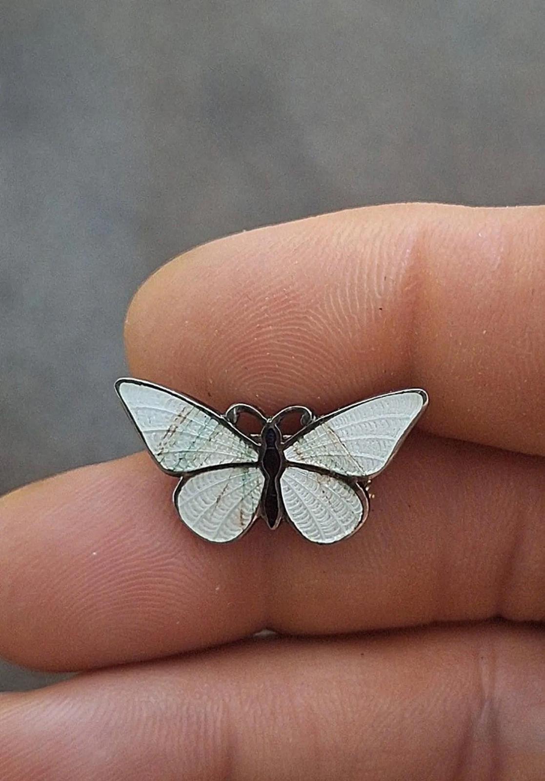 Enamel butterfly pin brooch with iridescent white wings and dark body on finger.
