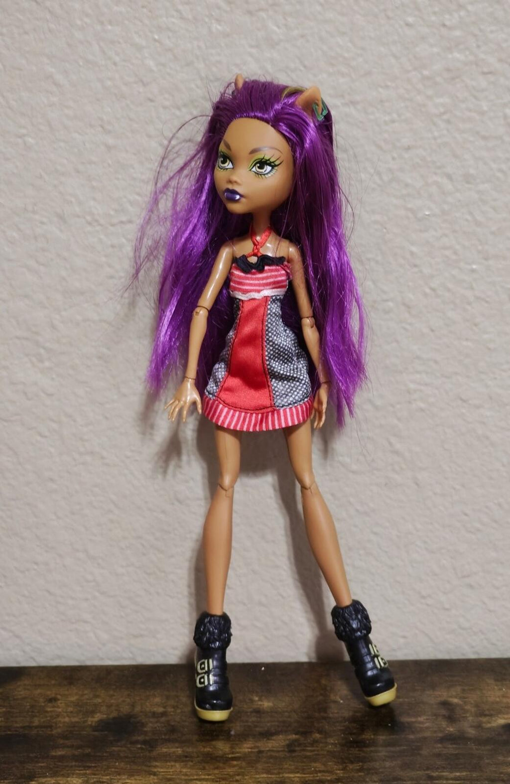 Purple-haired fashion doll in red dress with striped hem and black ankle boots