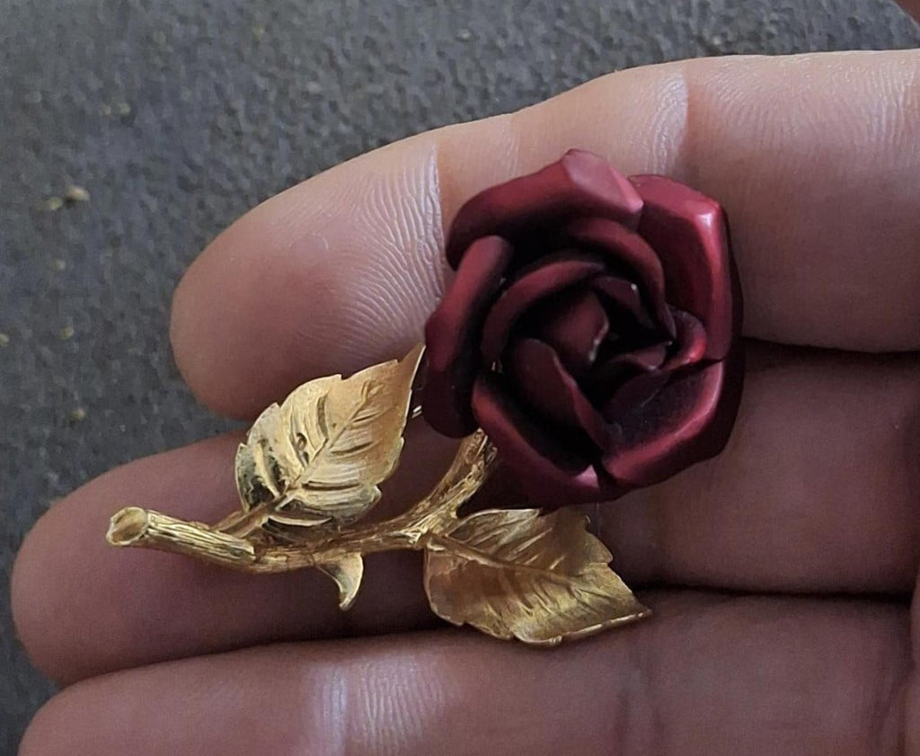 Gold-tone red rose enamel pin brooch, hand-held close-up of rose and leaves.