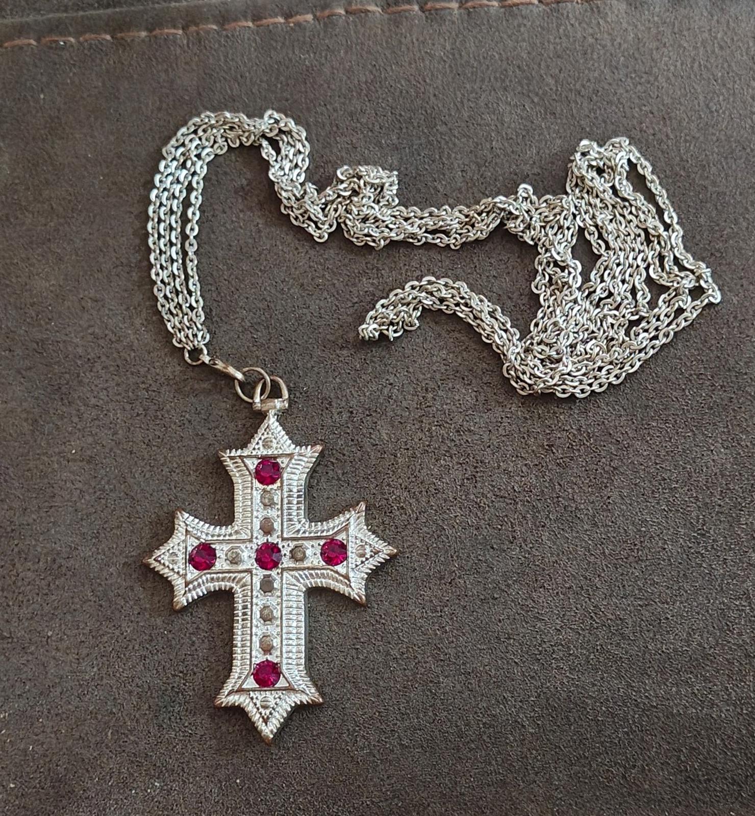 Silver tone cross pendant necklace with red rhinestones laid flat with metal chain