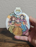 Round hanging ornament with illustrated prairie-style girls and small toy cart