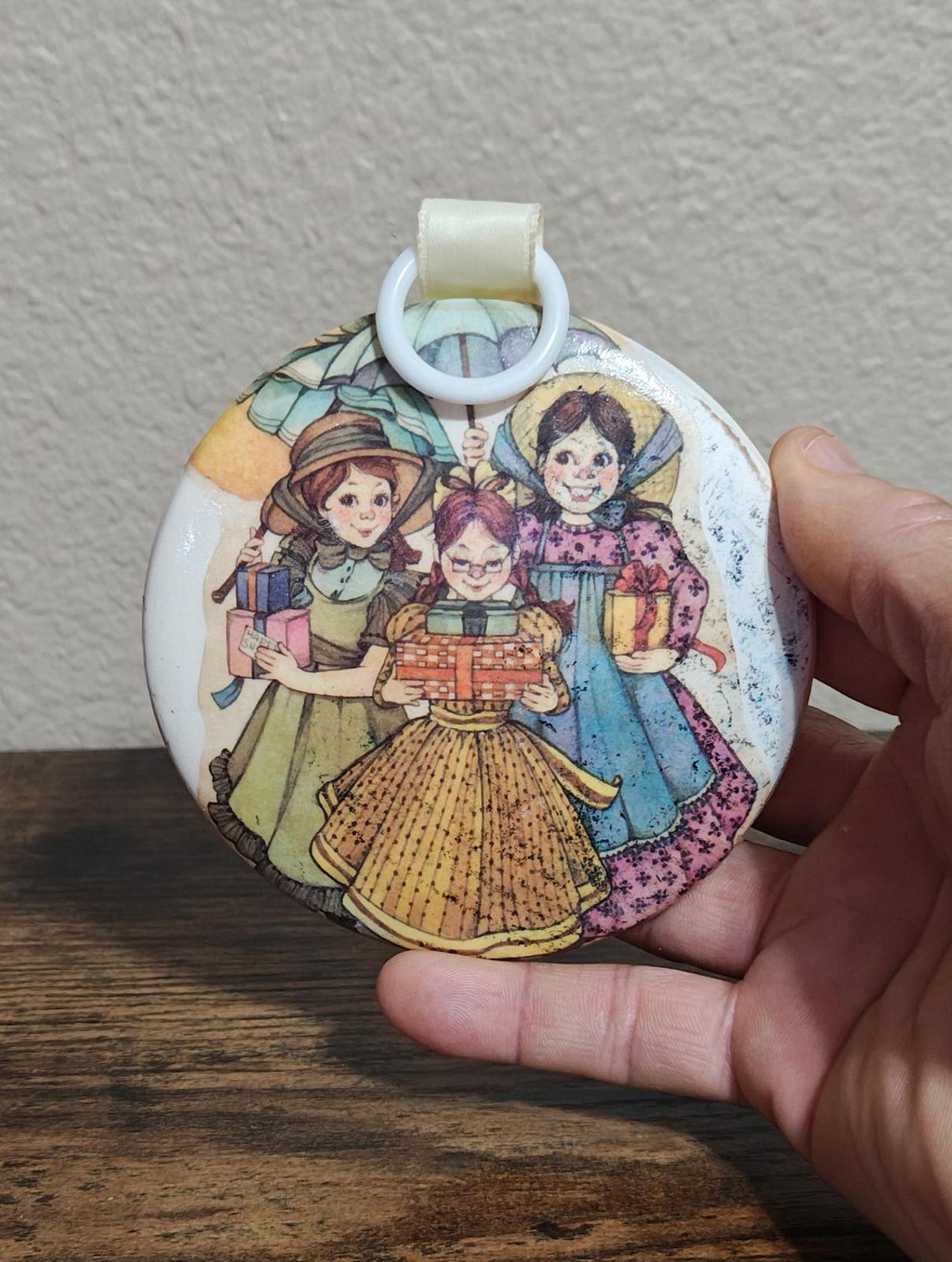 Round hanging ornament with illustrated prairie-style girls and small toy cart