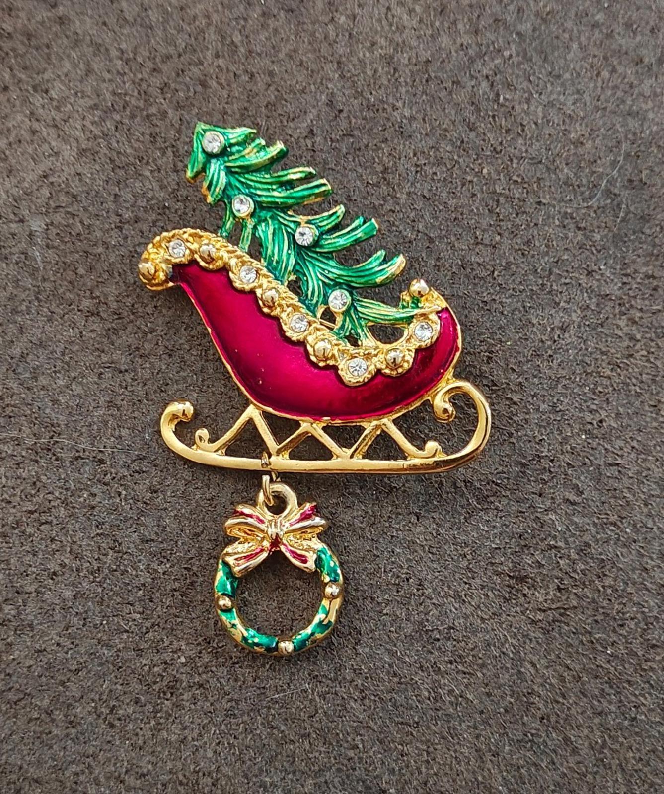 Enamel Christmas sleigh pin with red body, green tree, gold trim, and dangling wreath.