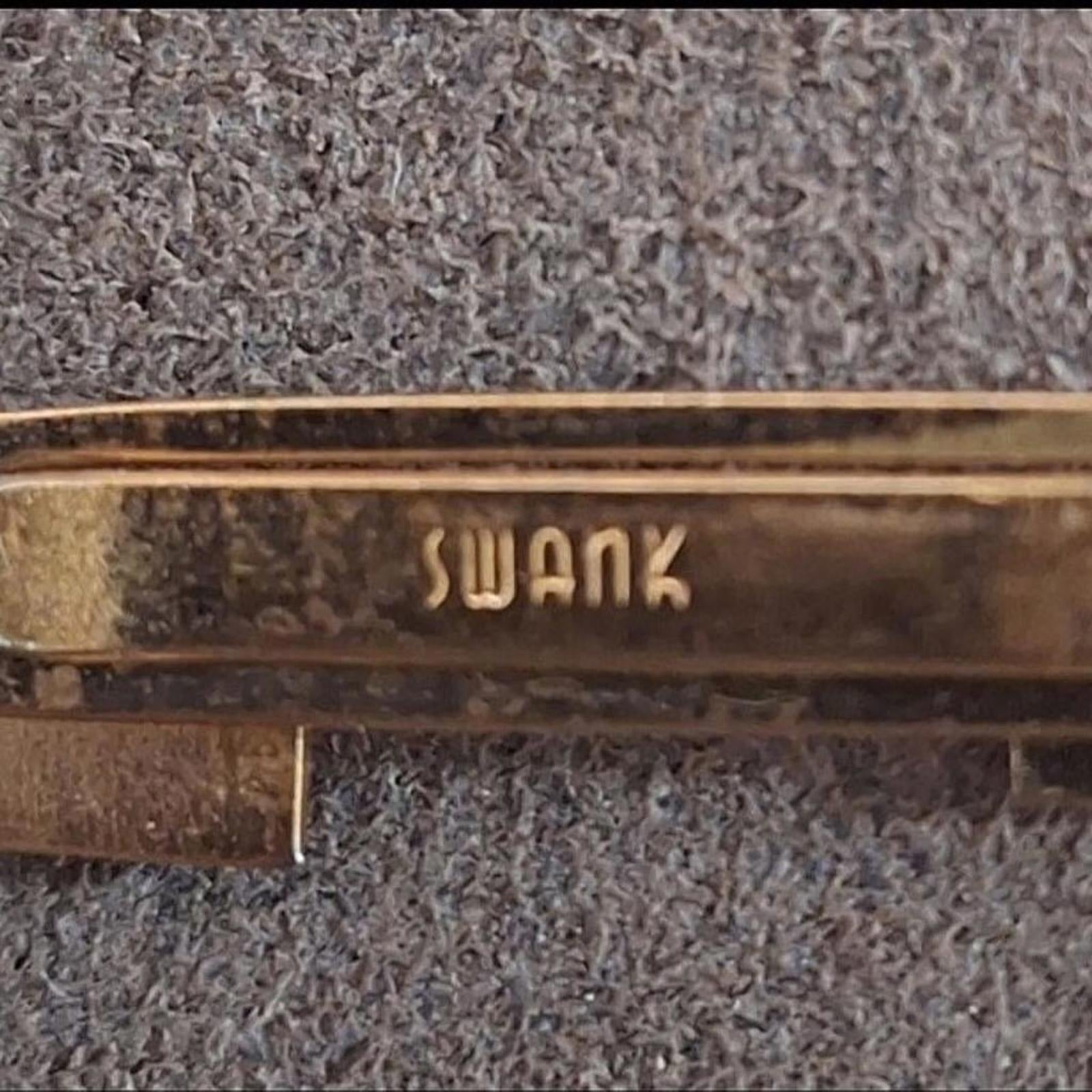 Gold pirate sword tie clip bar with partial engraved text on the bar