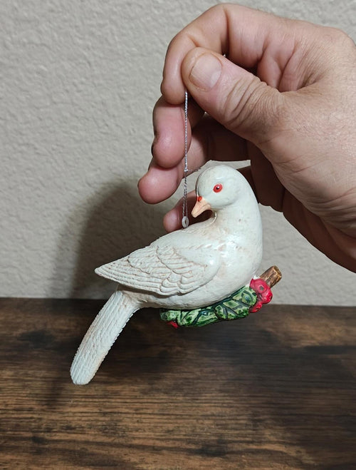 White plastic dove Christmas ornament held in hand, red eye and green scarf with bell.