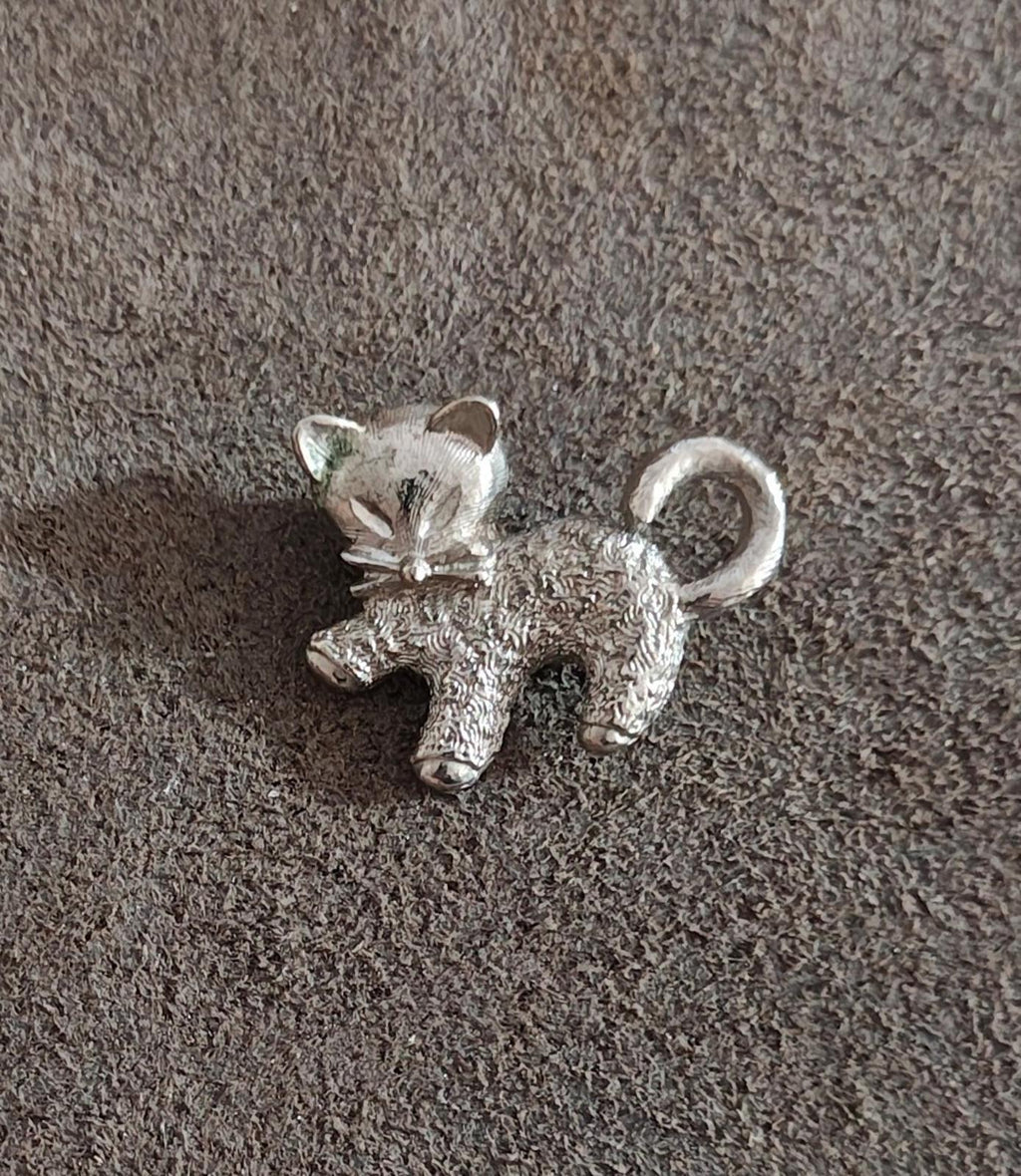 Silver-tone cat brooch pin with textured finish and curled tail on fabric.