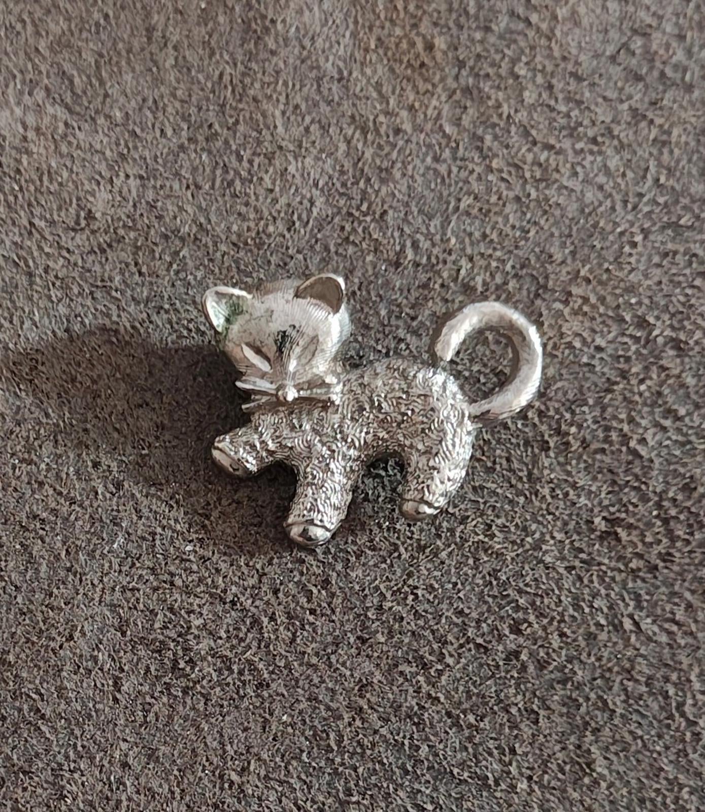Silver-tone cat brooch pin with textured finish and curled tail on fabric.