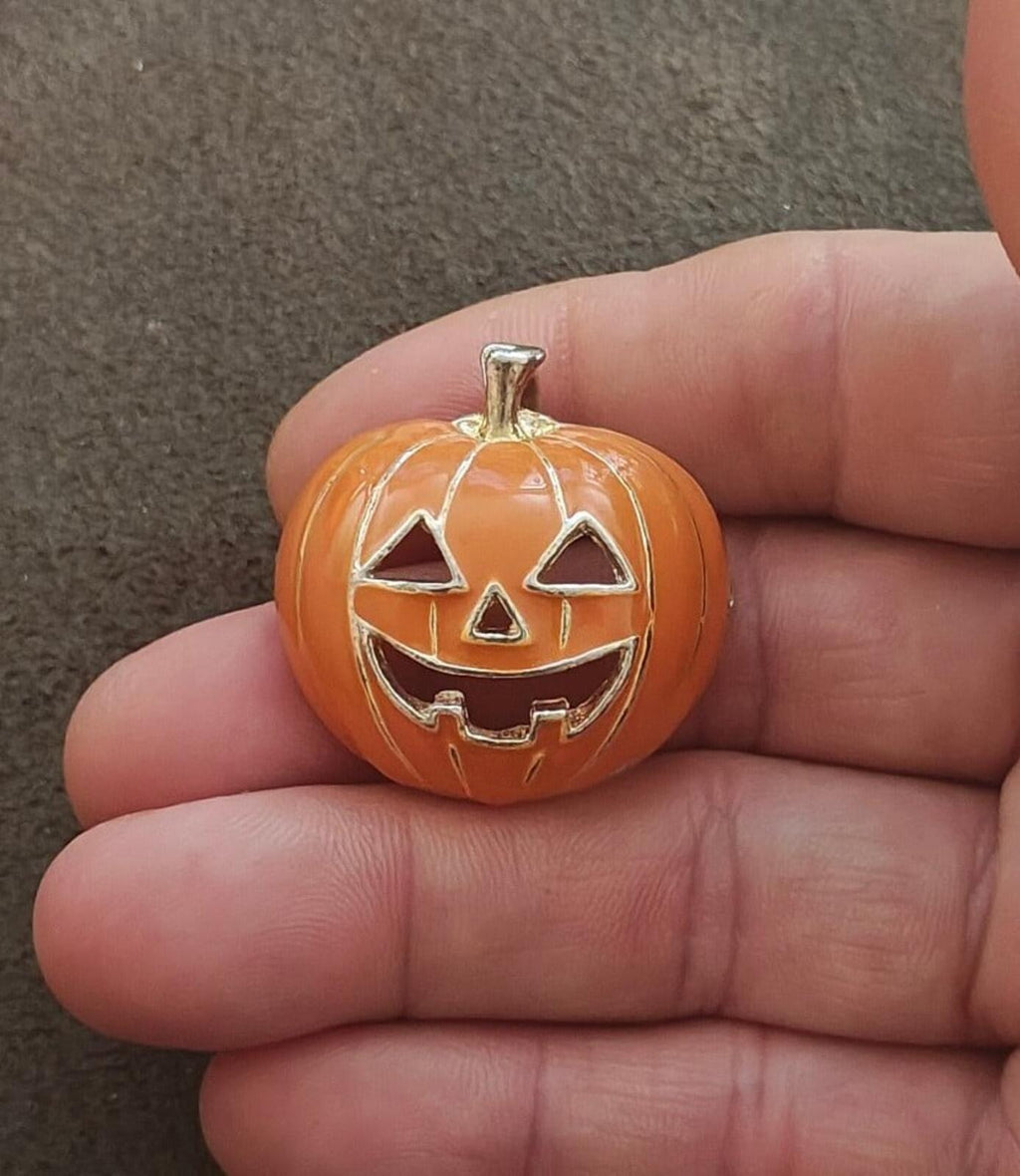 Orange pumpkin brooch pendant held in hand, silver-tone jack-o'-lantern face