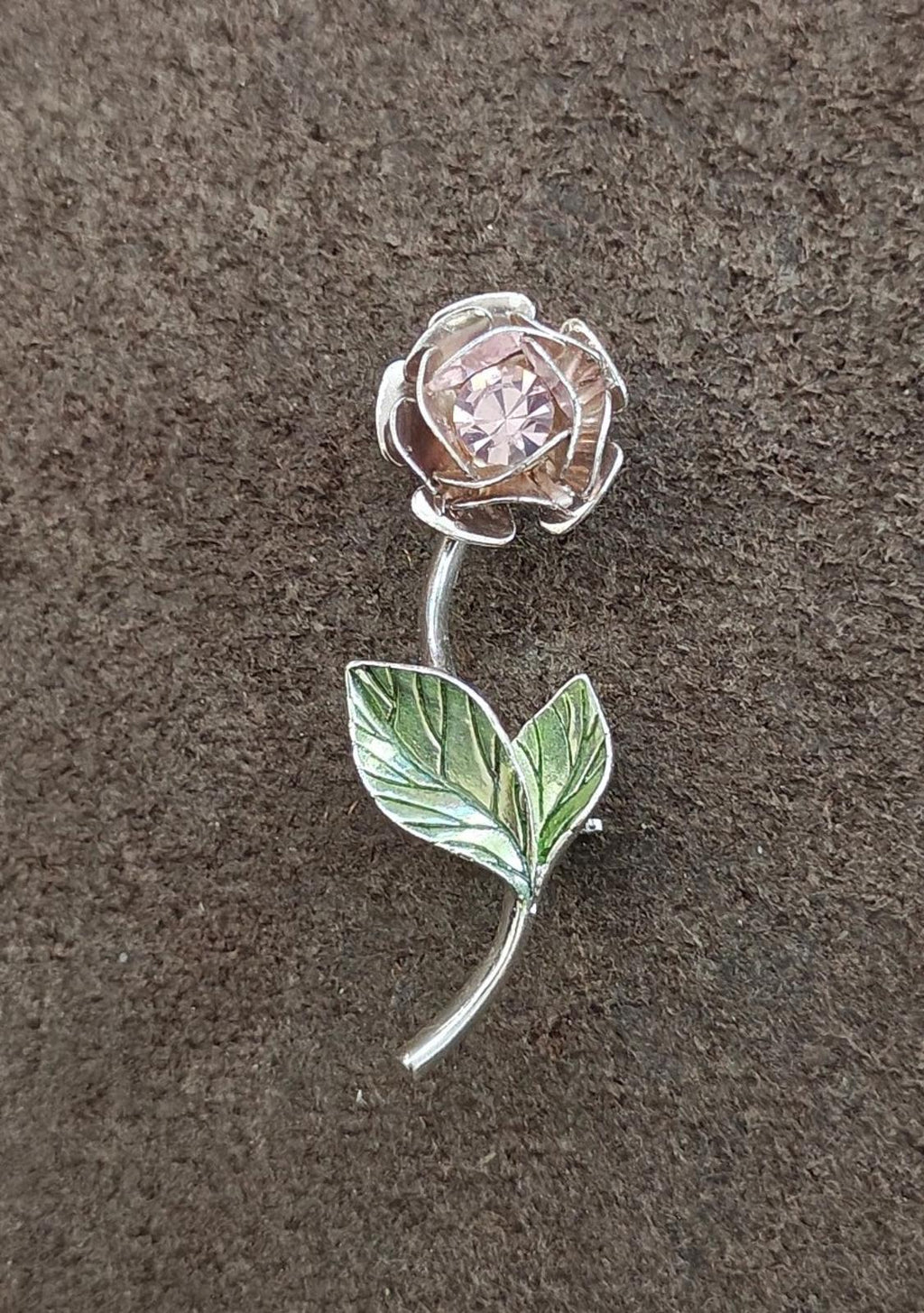 Silver-tone brooch with rhinestone flower head and green enamel leaf on a long curved stem