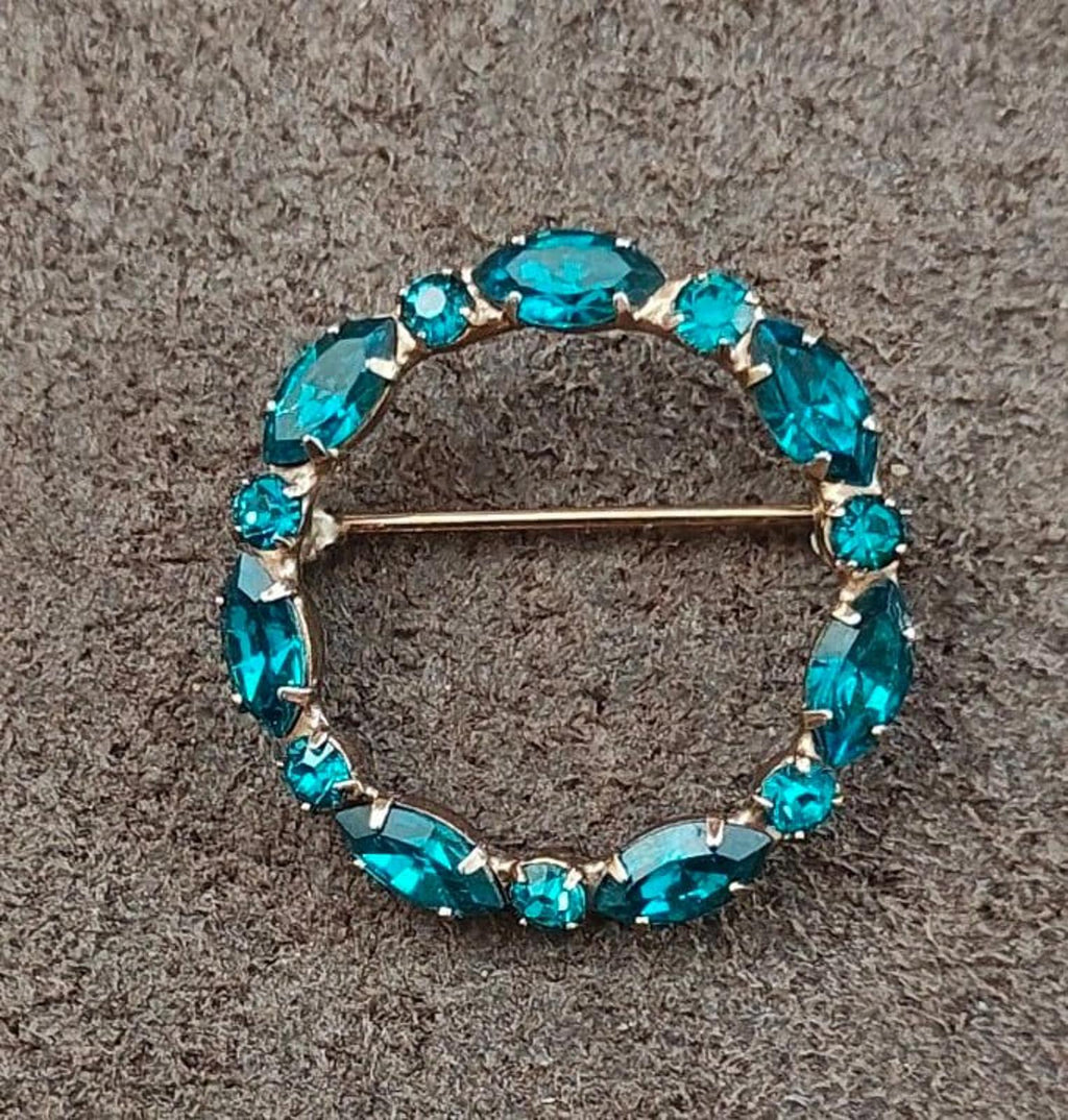 Aqua blue rhinestone oval circle brooch pin with gold-tone bar clasp, angled view