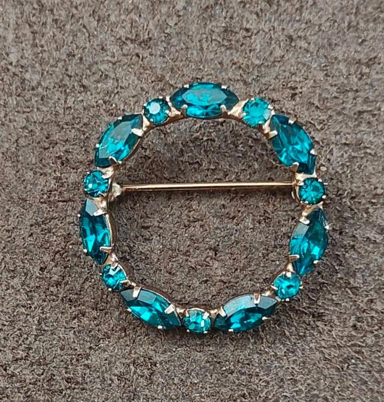 Aqua blue rhinestone oval circle brooch pin with gold-tone bar clasp, angled view