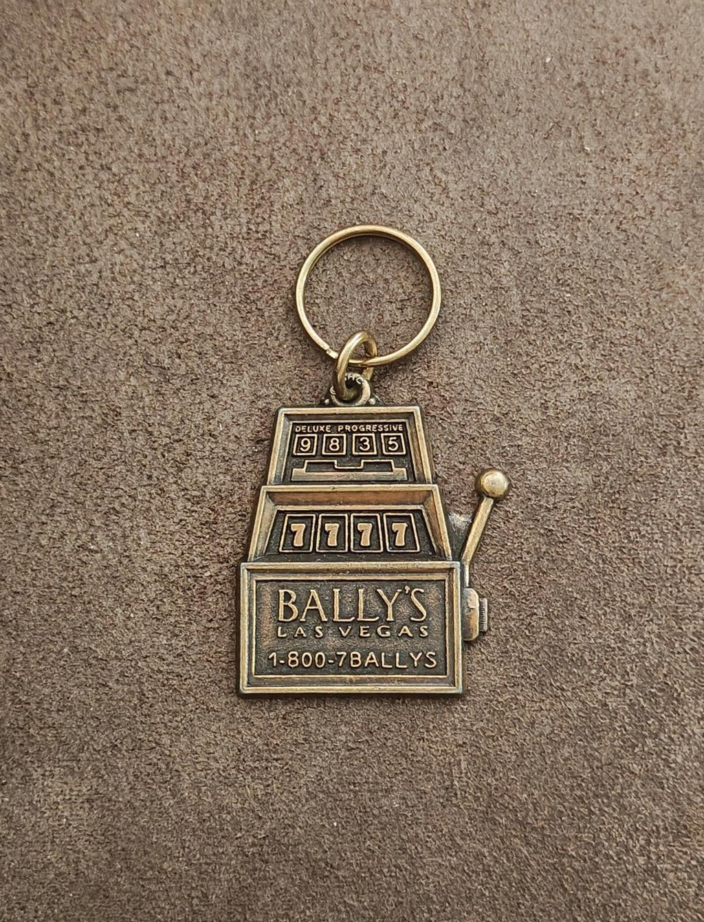 Brass Bally's Las Vegas slot machine keychain on gray surface with keyring