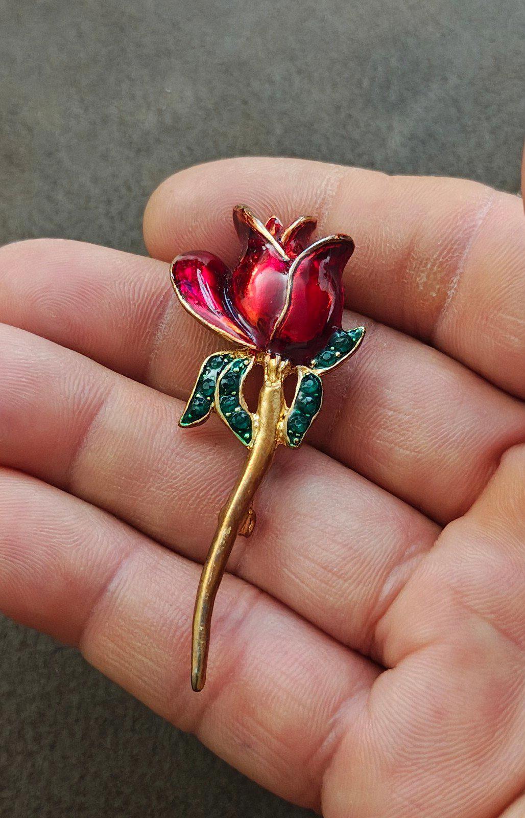 Red flower brooch with green rhinestone leaves and gold-tone stem, close-up on hand