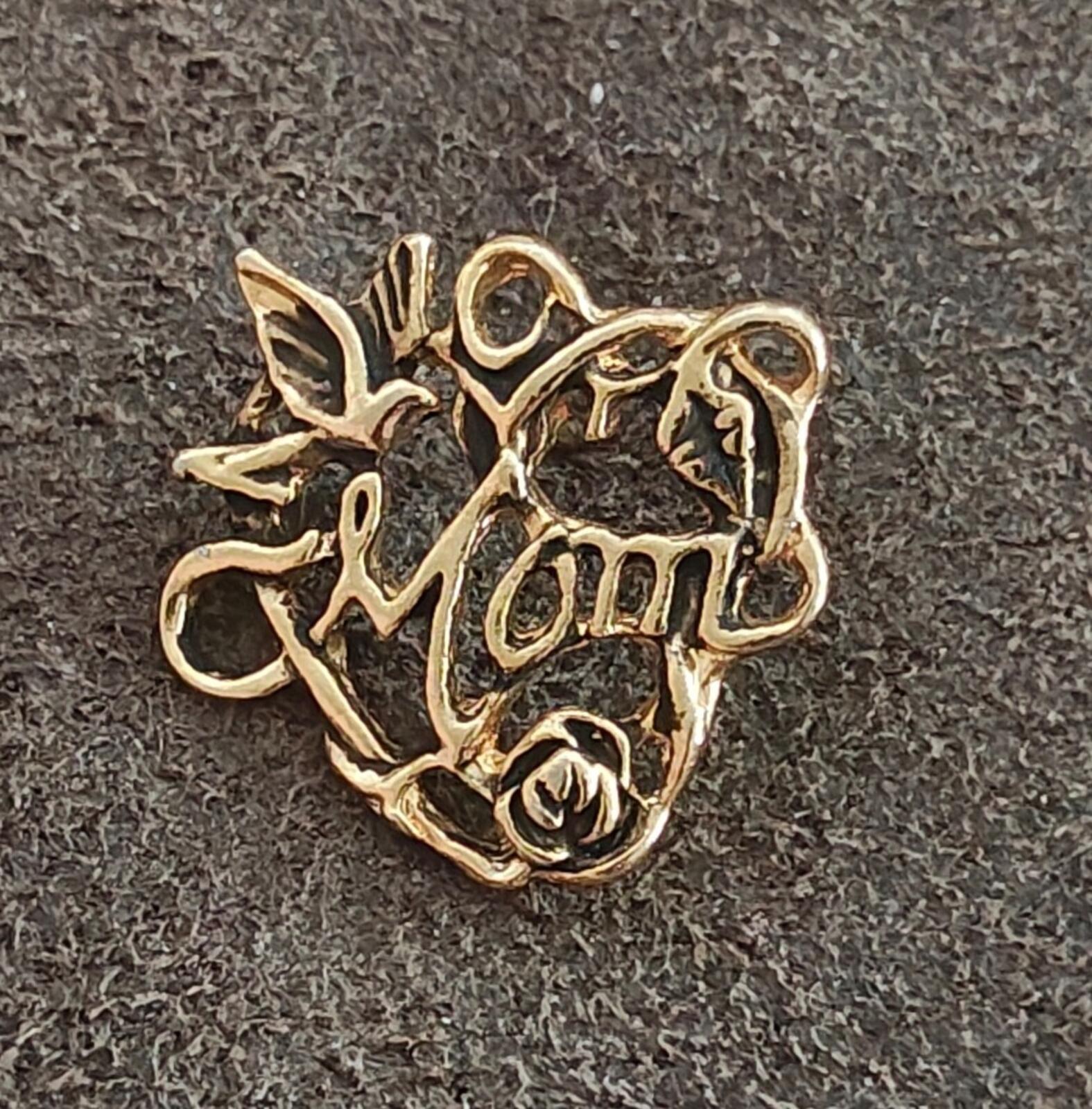 Gold-tone floral heart pin close-up with rose and “Mom” text on dark background
