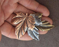 Layered leaf pin brooch with brown, gold, and silver leaves, held in hand