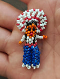 Seed bead figure brooch with white/red hat, orange face, and blue beaded dress