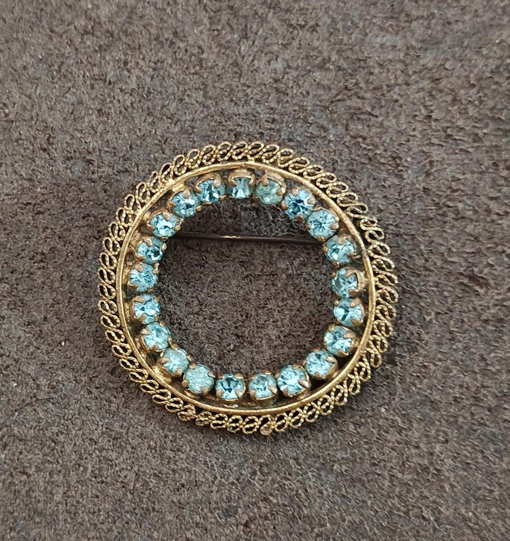 Gold-tone round brooch with blue stones and textured ornate frame