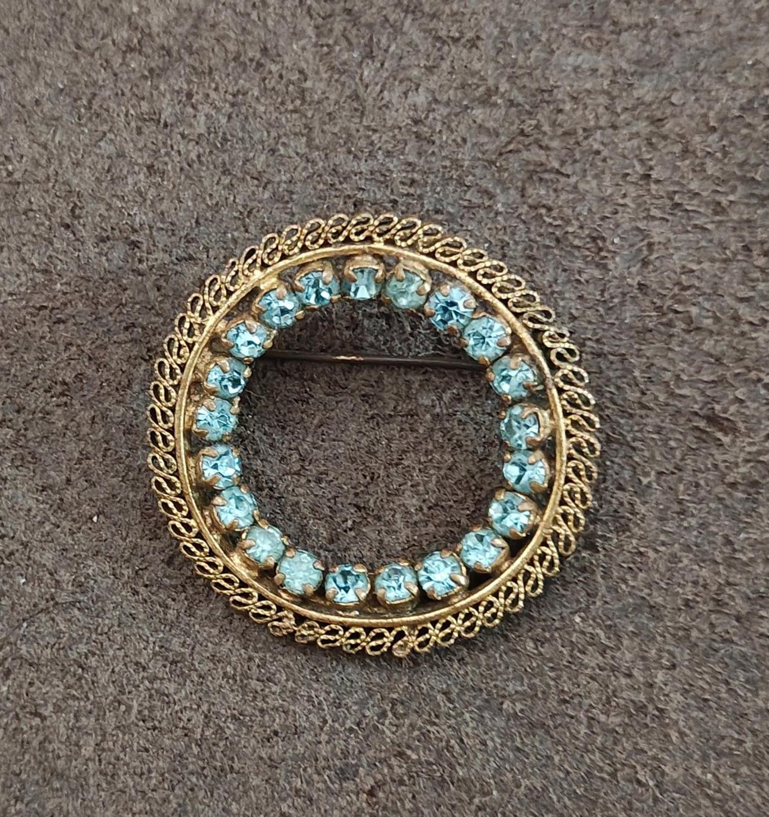 Gold-tone round brooch with blue stones and textured ornate frame