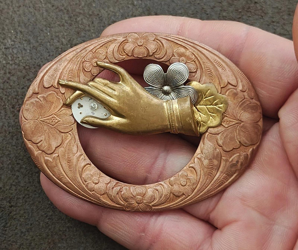 Bronze round steampunk brooch held in hand, engraved rim with gold bird and gray flower