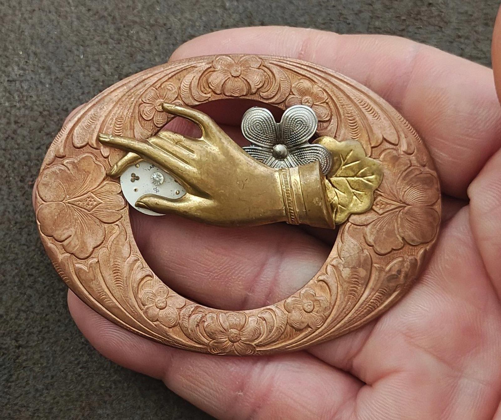 Bronze round steampunk brooch held in hand, engraved rim with gold bird and gray flower