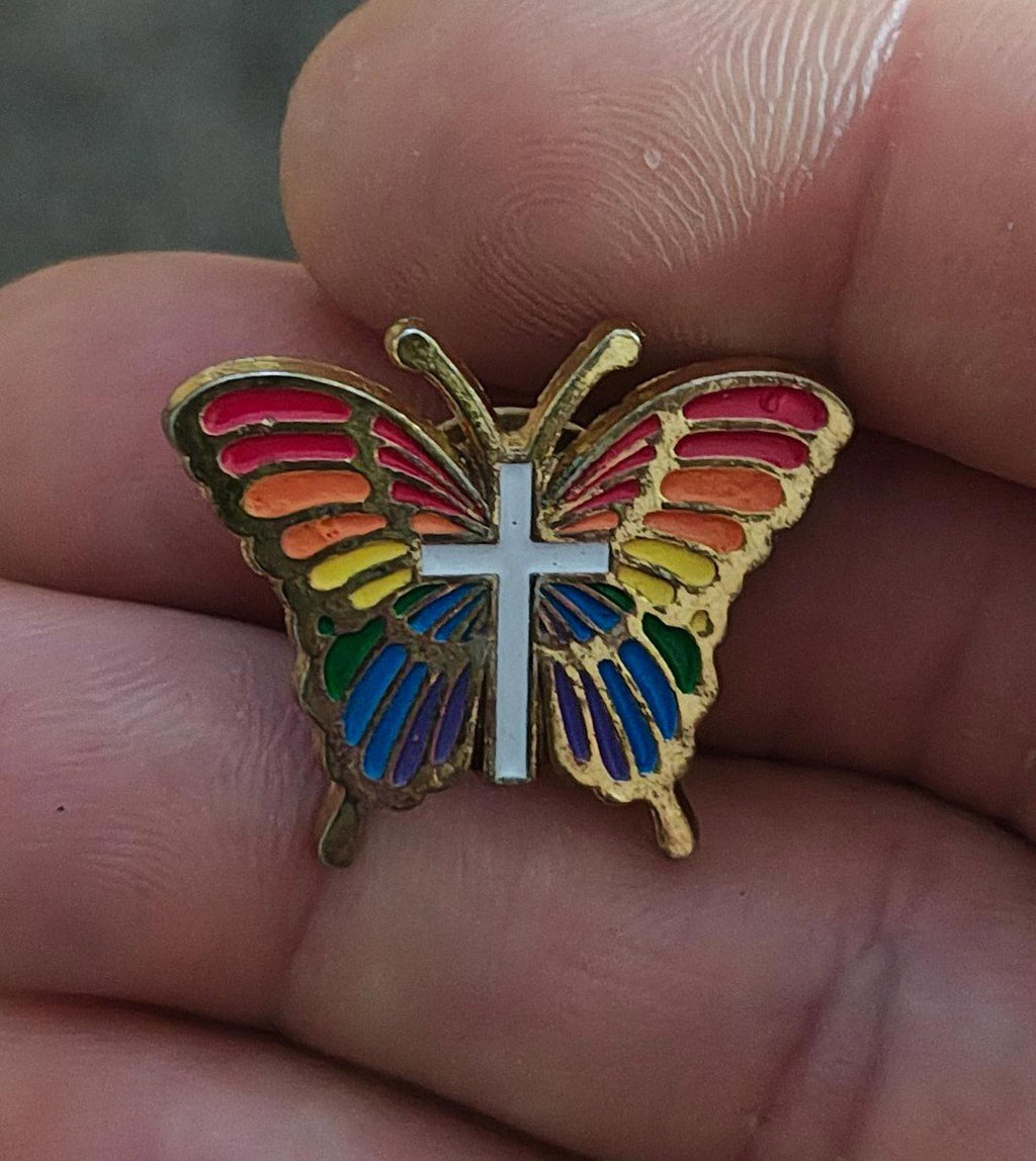 Rainbow butterfly enamel pin with white cross, multicolor wings, gold-tone frame