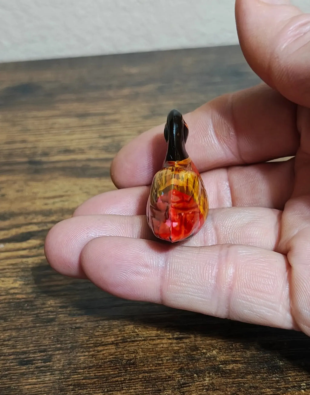 Small hand-painted wooden duck figurine held in fingers, narrow side detail view.