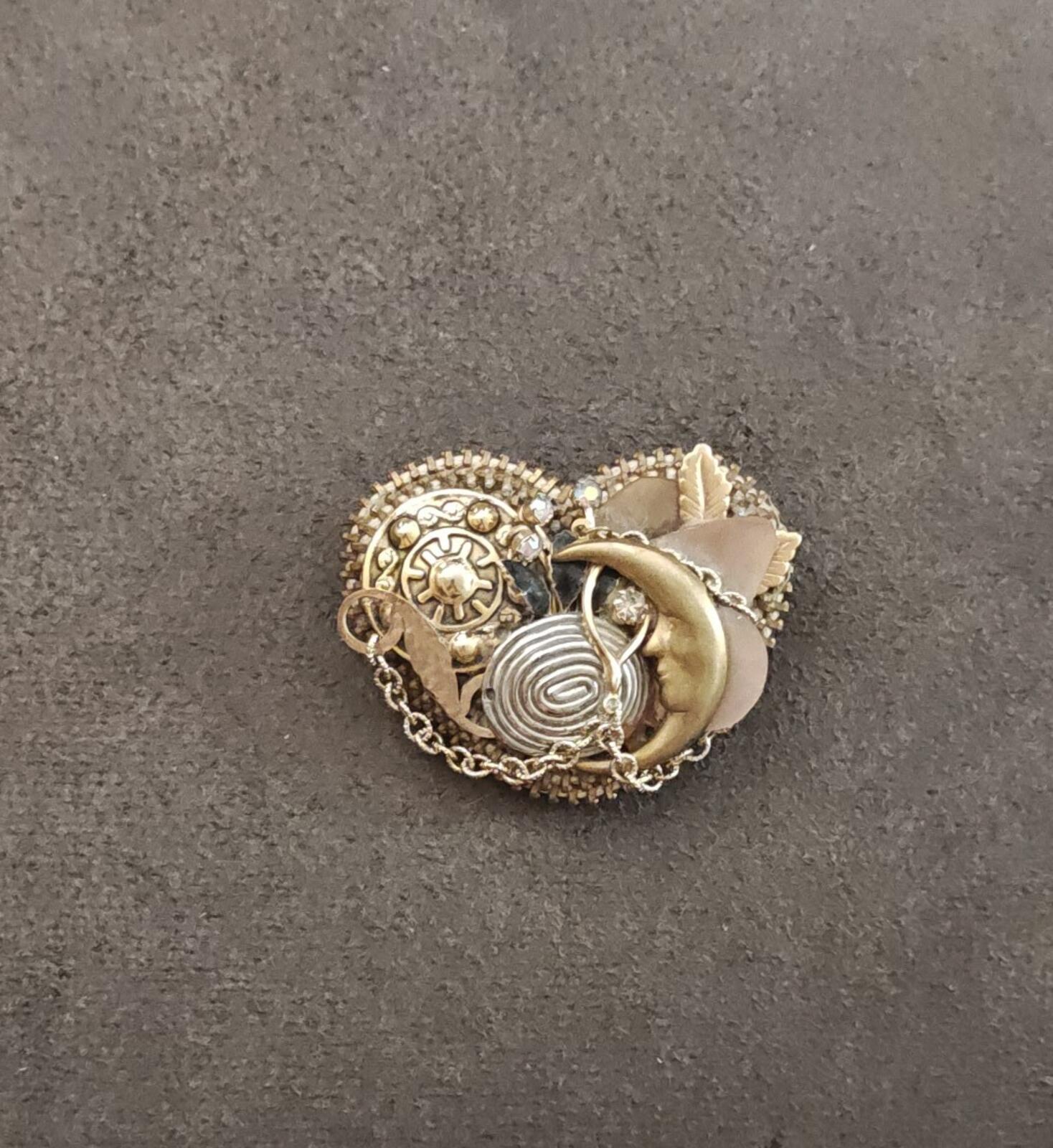 Gold tone celestial charm brooch featuring moon and spiral center design with chain trim.