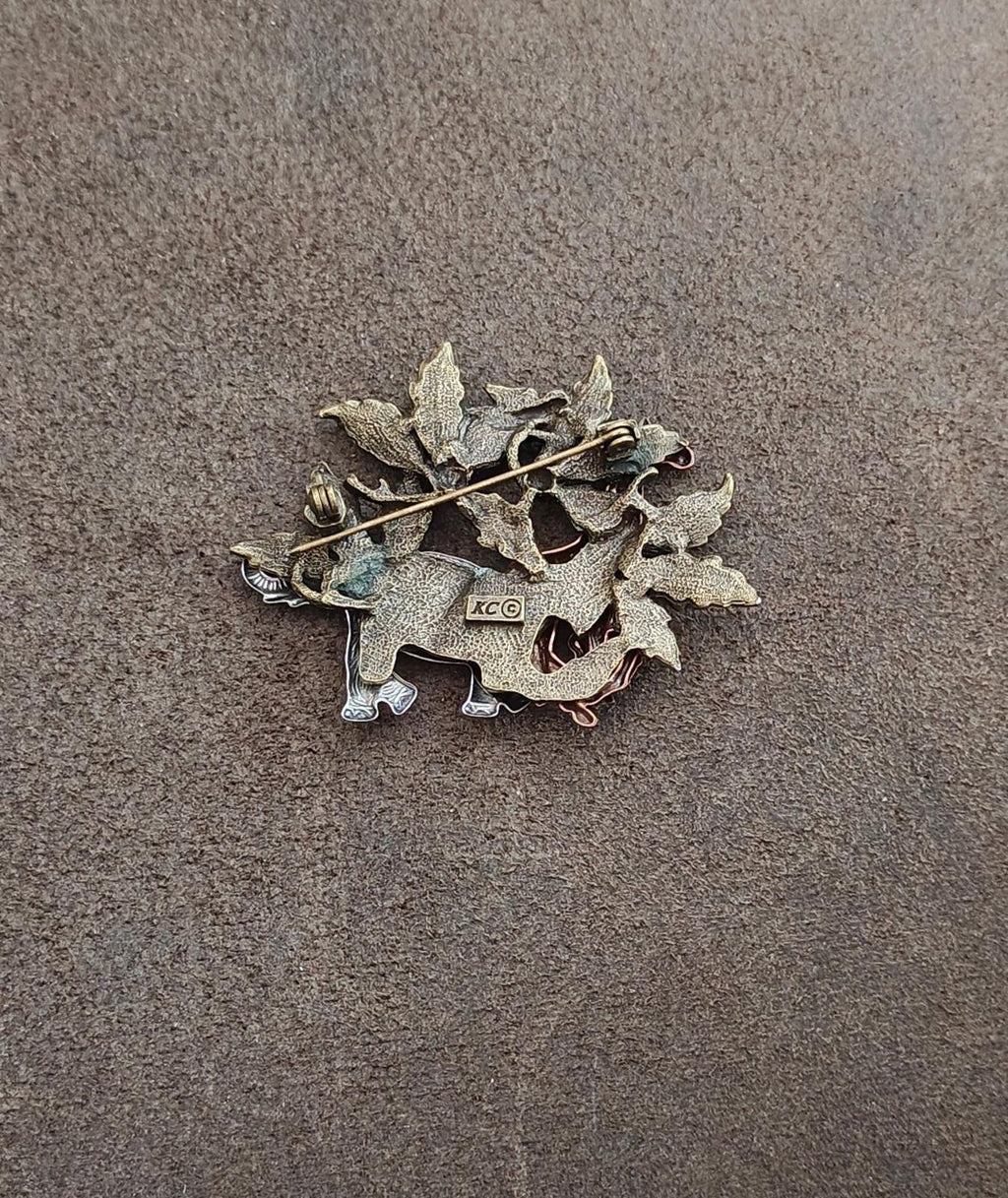 Back of safari animal brooch with leafy frame and "XC" hallmark at center