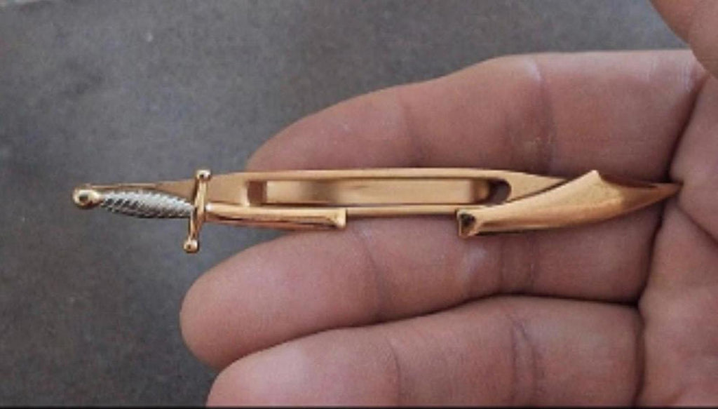 Gold pirate sword tie clip bar held in hand, centered window and blade tip visible