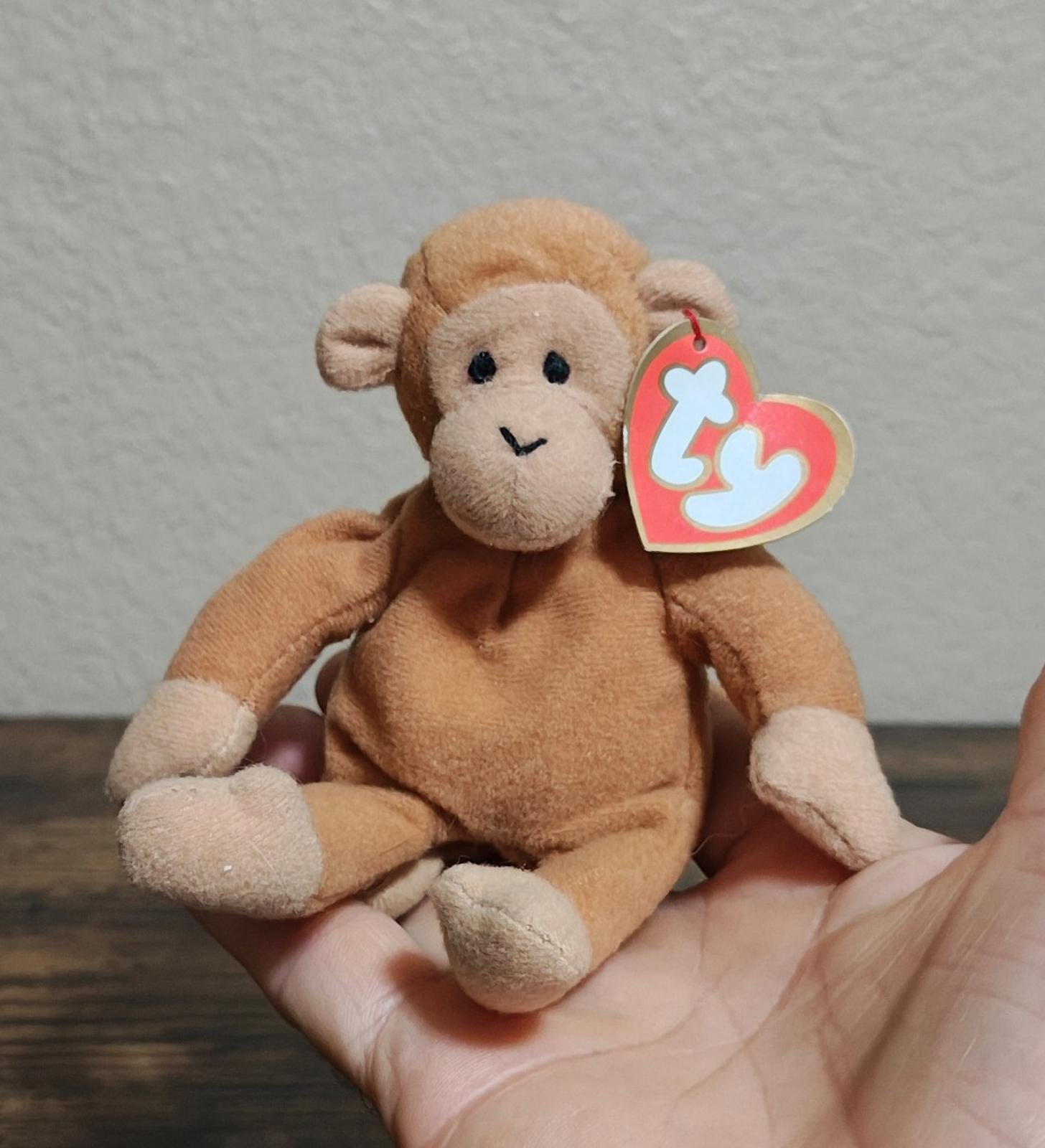 Brown Ty Beanie Babies plush monkey with heart tag, sitting in open hands