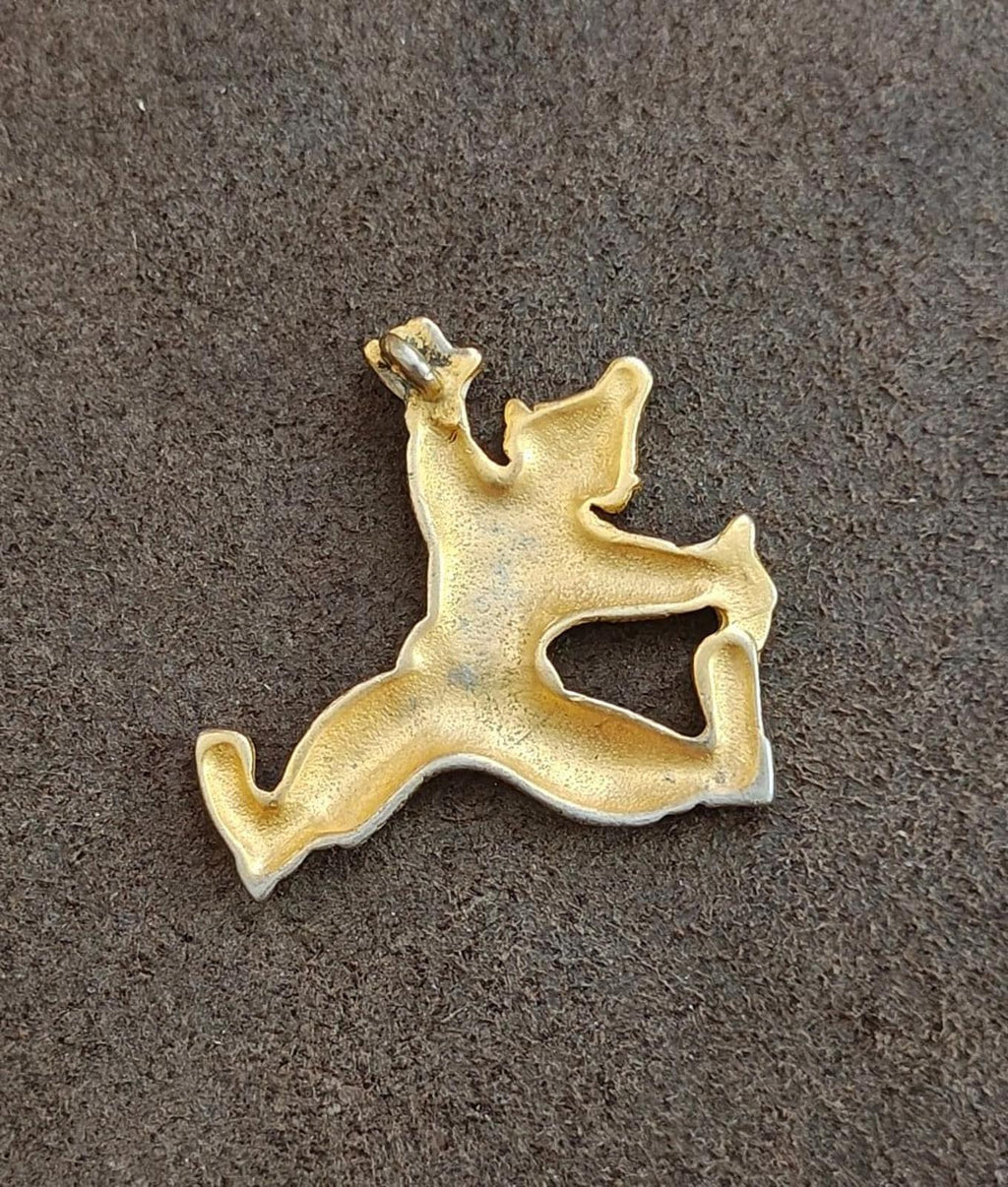 Gold tone clowning around pendant back view on gray surface, white enamel detail at limbs