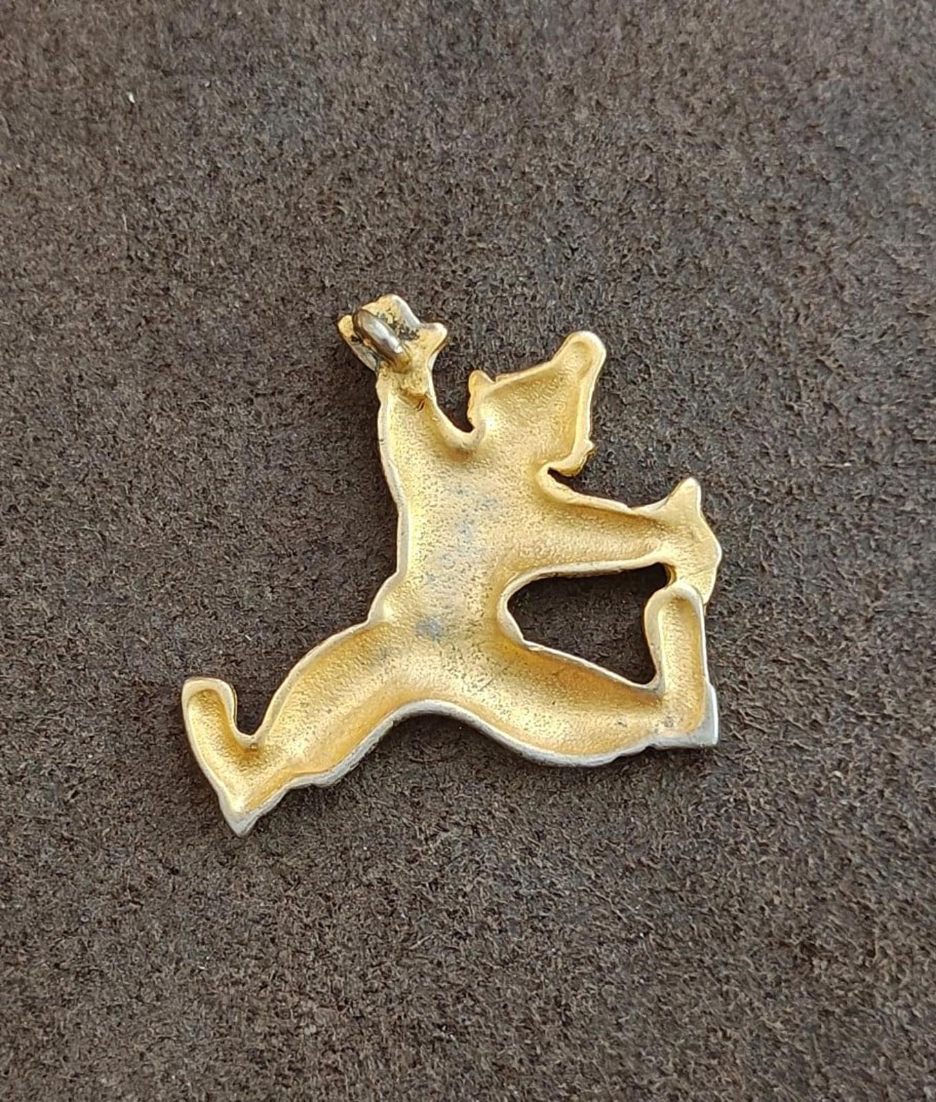 Gold tone clowning around pendant back view on gray surface, white enamel detail at limbs