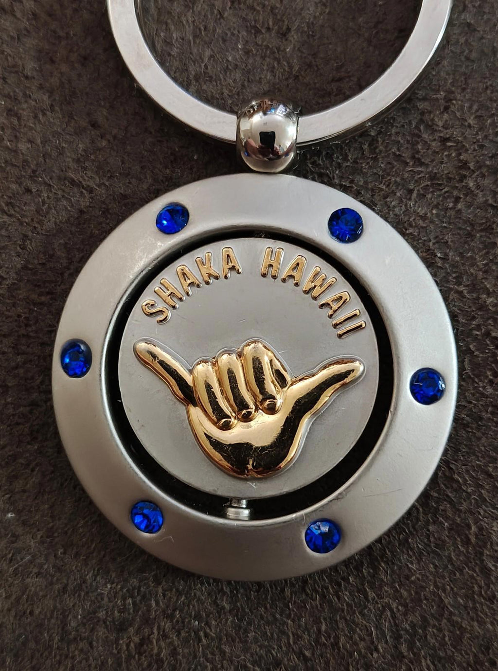 Two-tone round keychain with silver ring, blue accents, and gold Shaka Hawaii hand emblem.