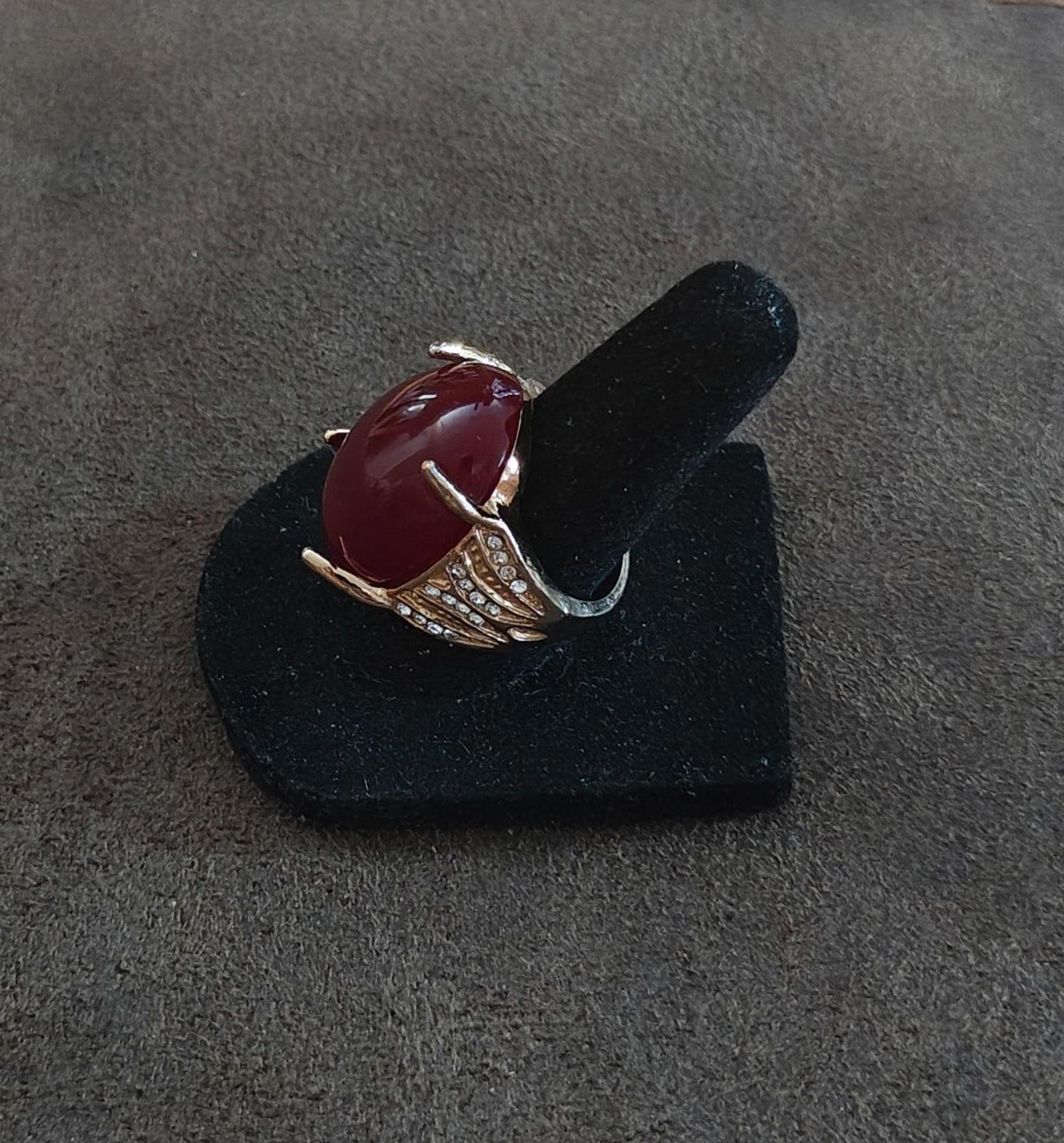 Red oval faux stone ring angled view with gold-tone band and clear rhinestone rows