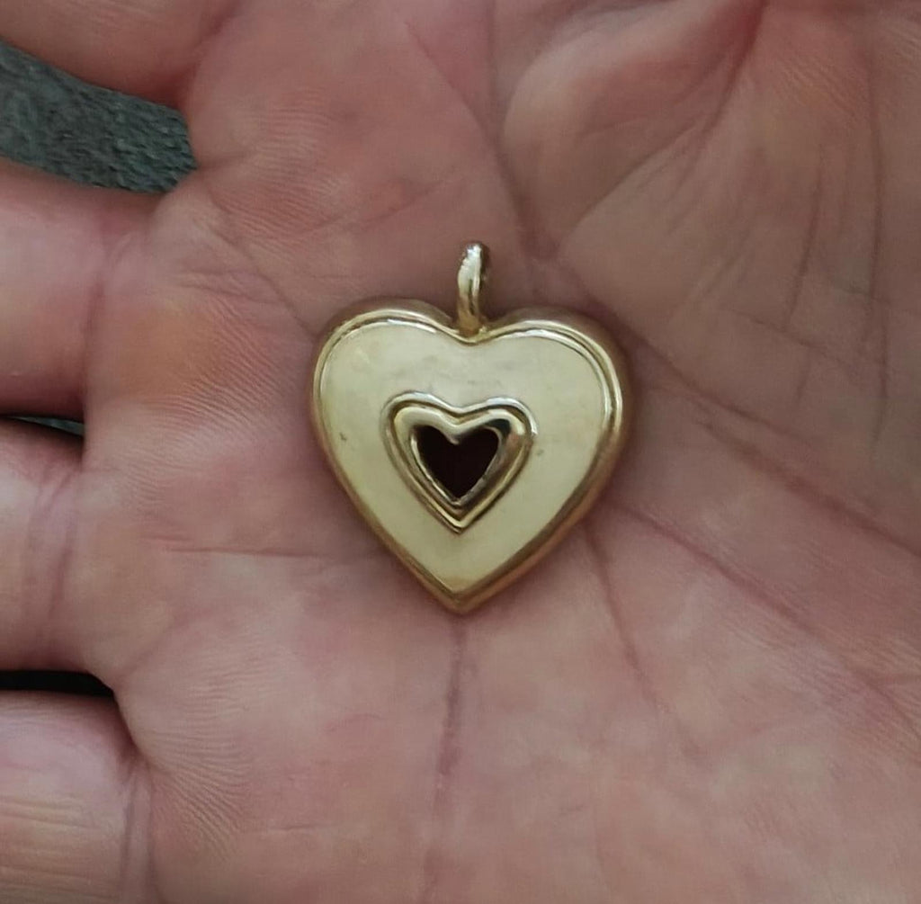 Gold tone heart pendant with white enamel and black heart inset, shown in hand