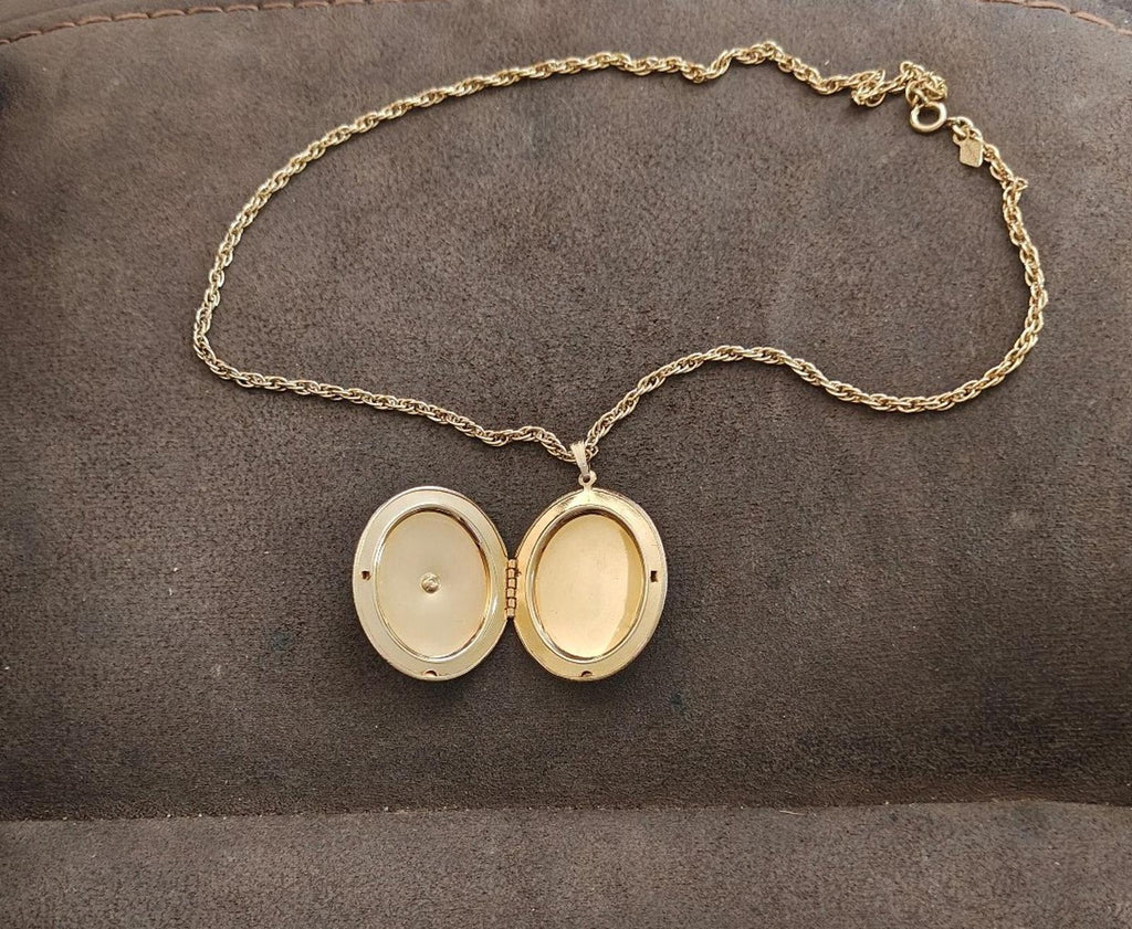Gold-tone locket necklace with chain, open oval pendant showing two cream interiors