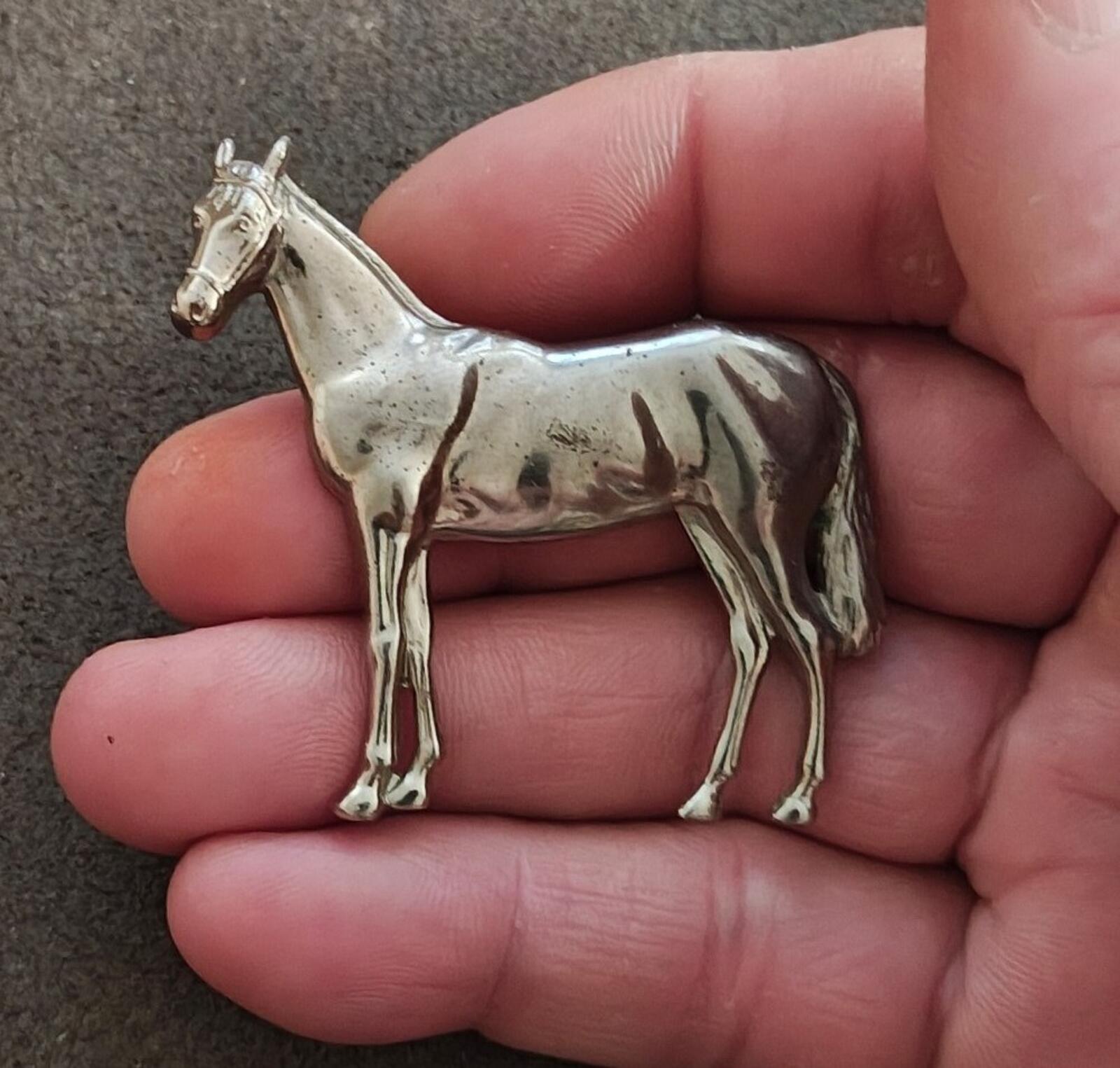 Silver-tone horse brooch with detailed standing horse figure, held in hand