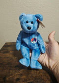 Blue bear plush with peace symbol patch, beanbag style, holding a red ribbon tag