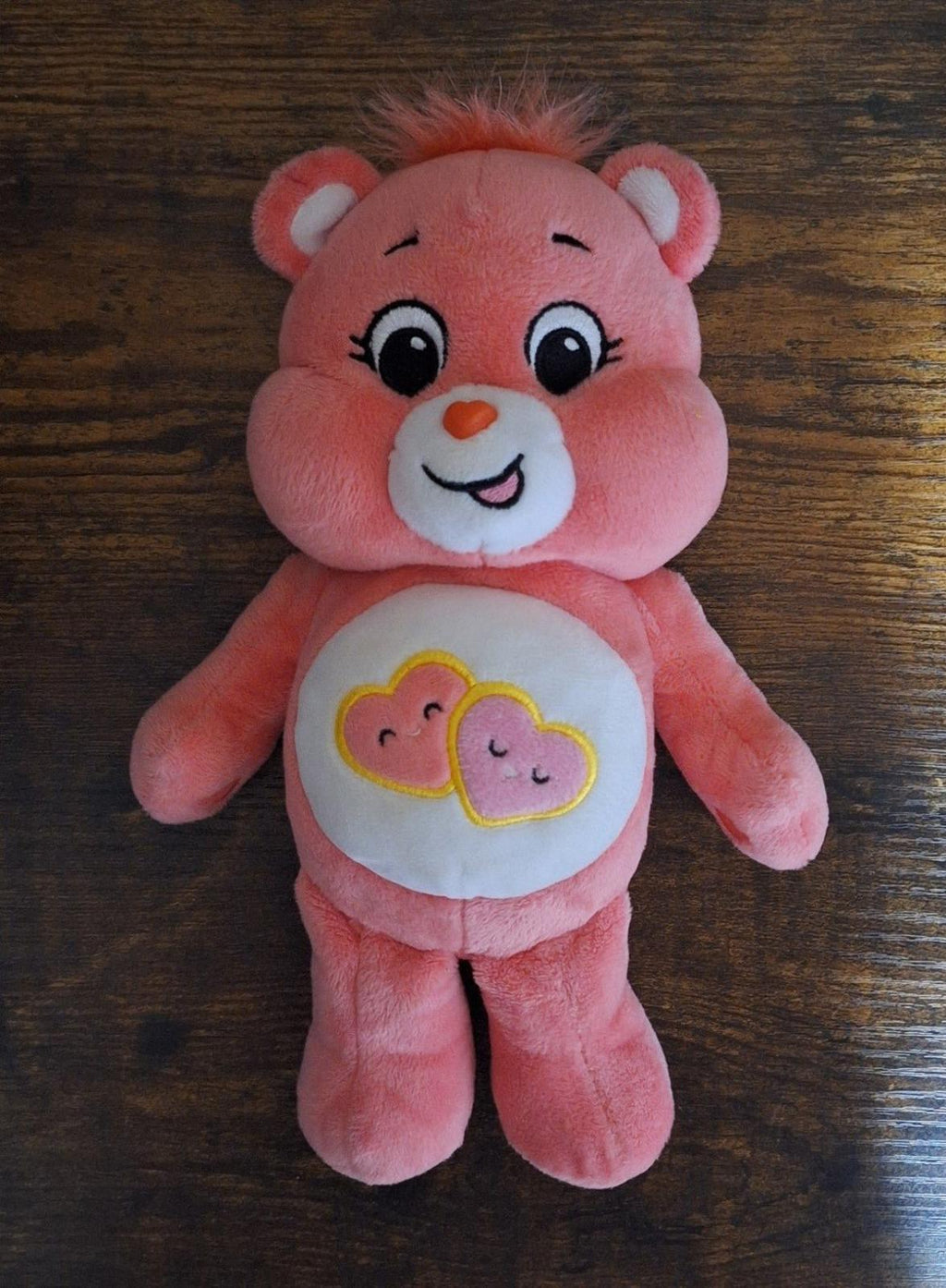 Pink plush bear standing with smiling face and heart belly emblem