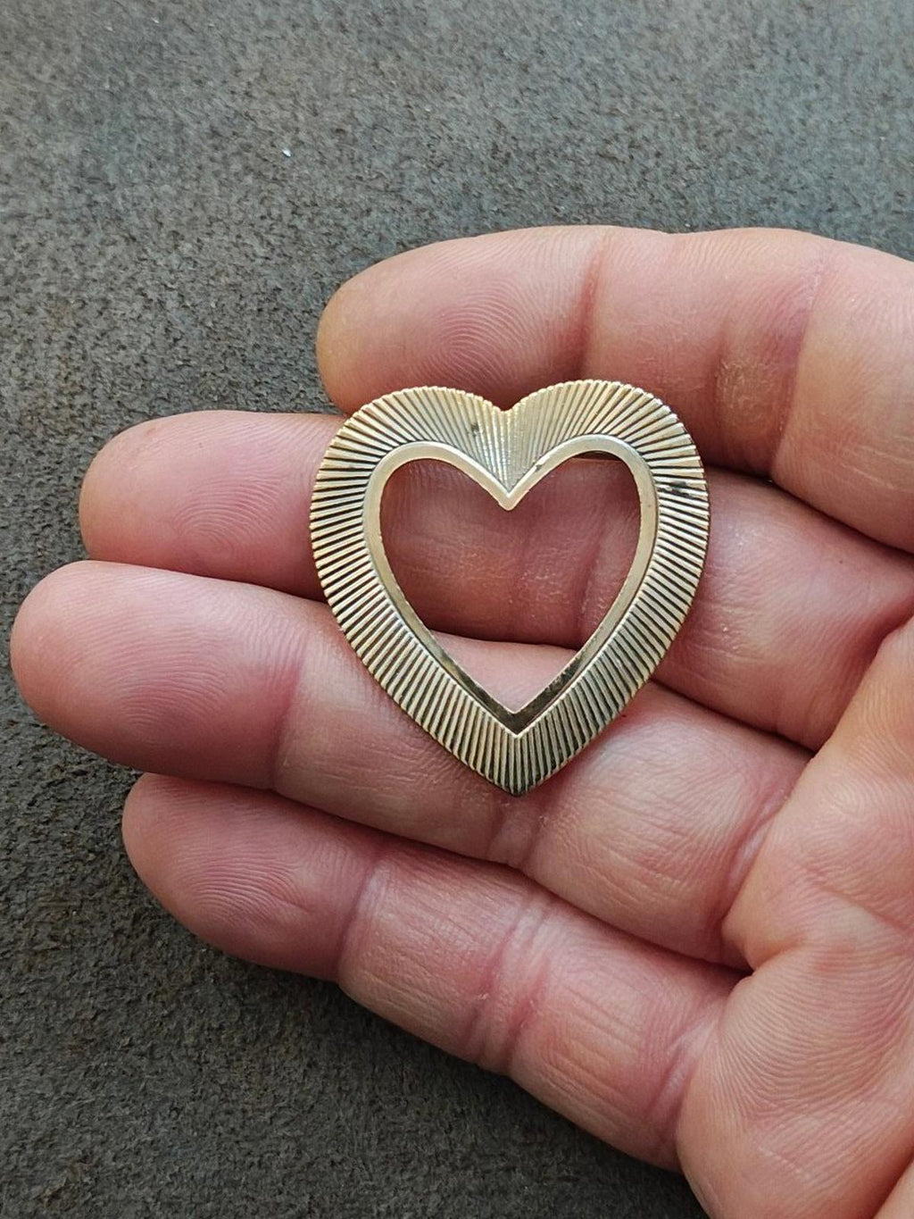 Gold heart-shaped brooch pin held in hand, textured ridges around the frame