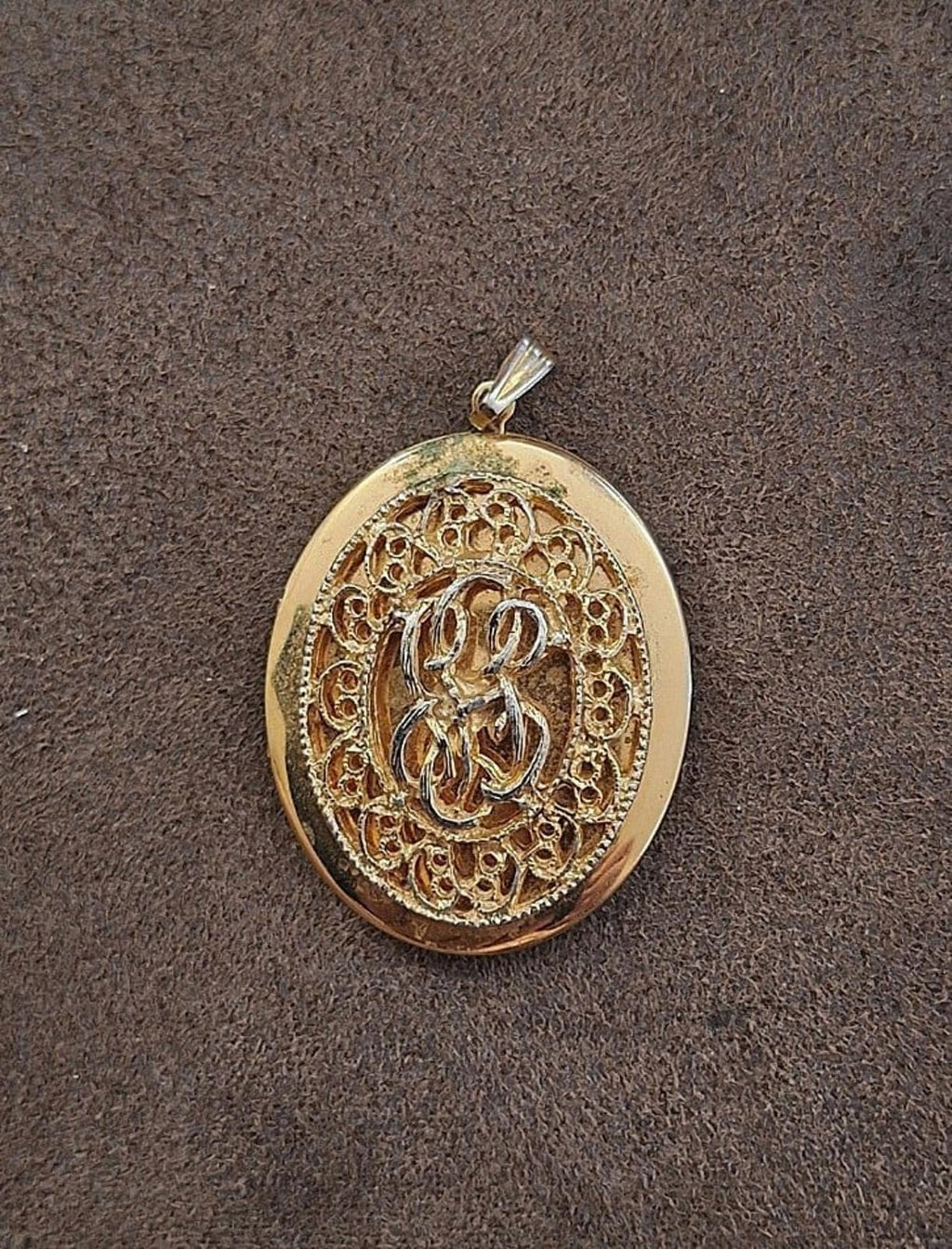 Gold tone oval filigree locket pendant front view with ornate inner design and bail.