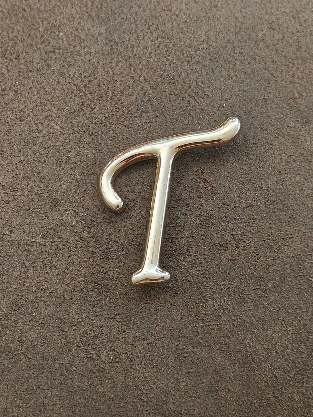 Silver-tone letter T pin/brooch, single-letter design on flat surface