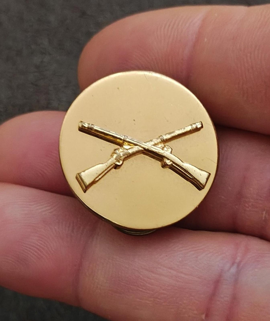 Gold circular brass pin with crossed rifles emblem, front view