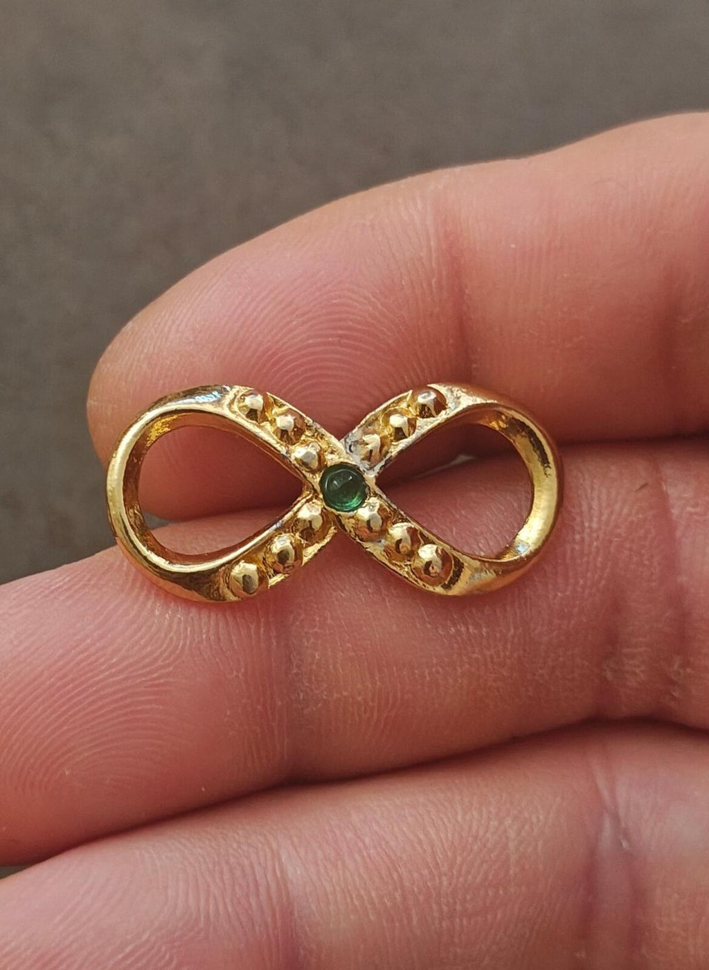 Gold infinity brooch with emerald center and surrounding clear prong-set stones